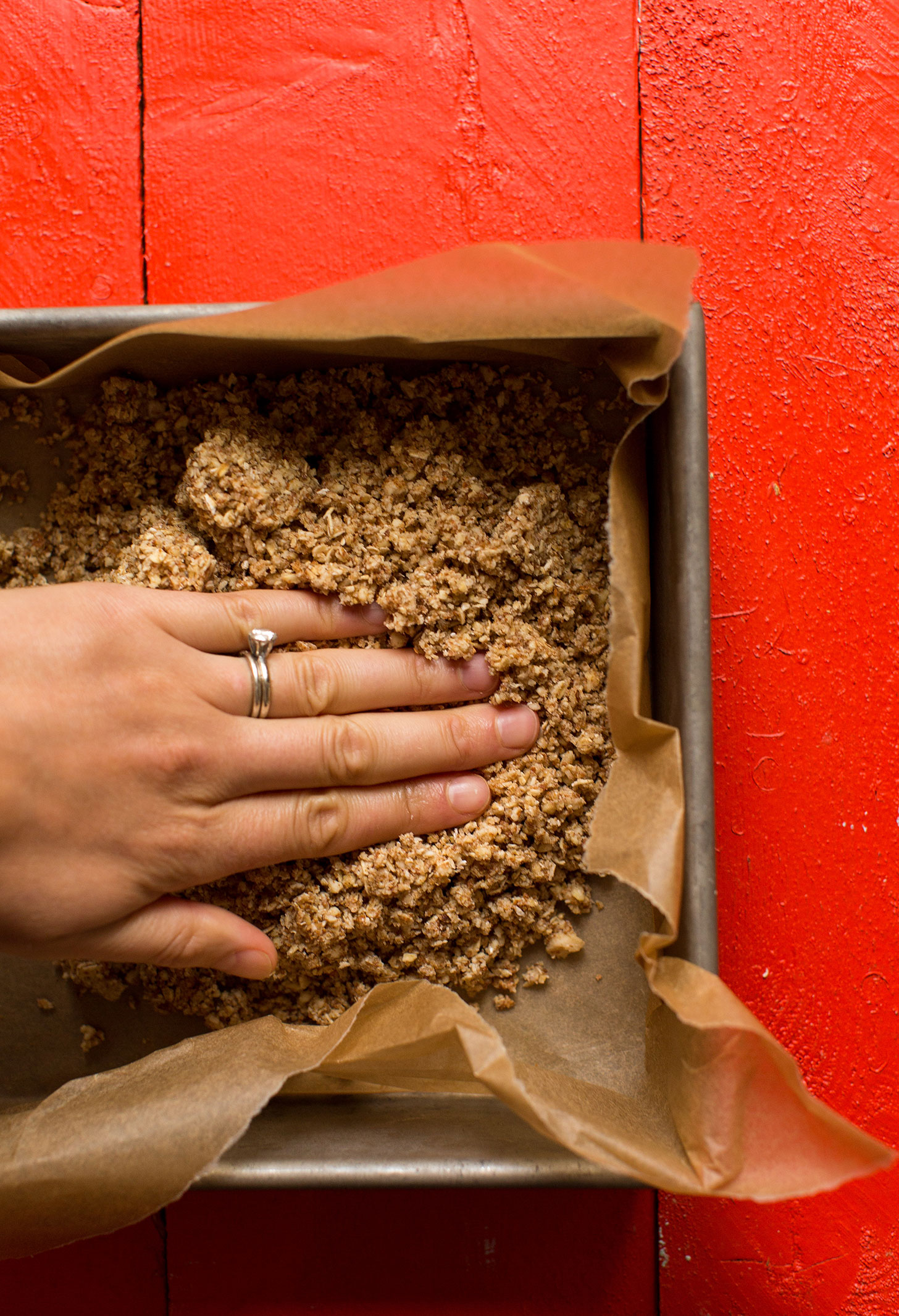 Pressing oat-almond crust ingredients into a parchment lined baking pan for gluten-free vegan apple pie bars