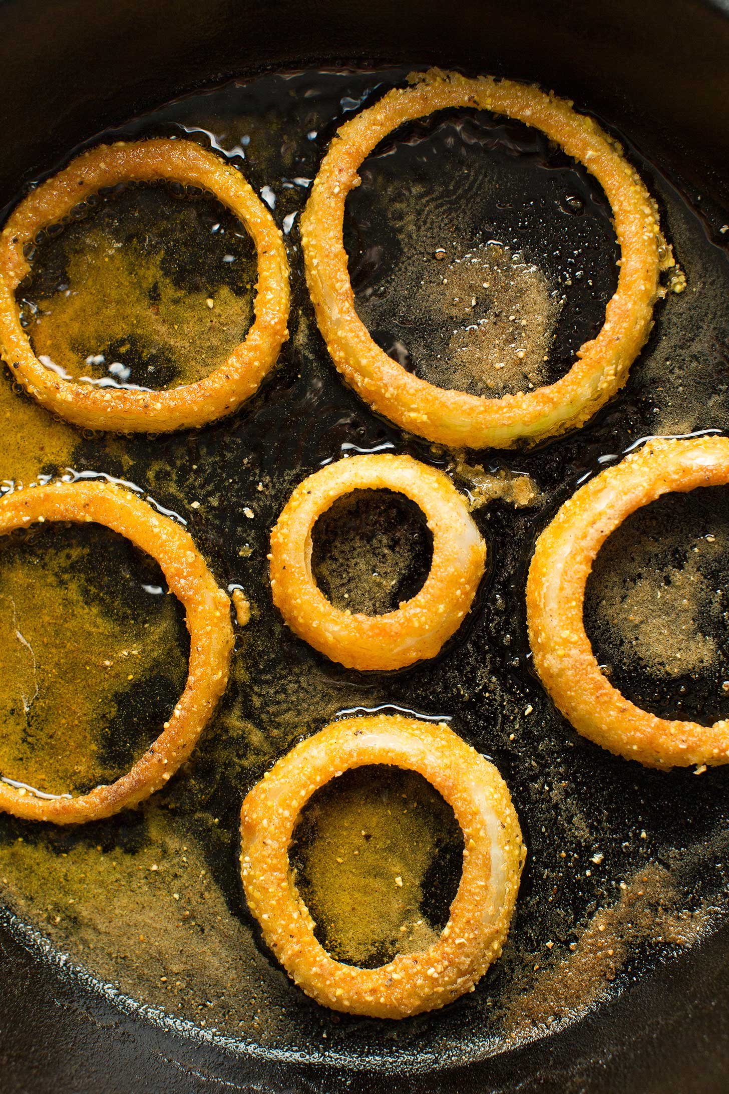 Gluten-free onion rings sizzling in a cast iron skillet