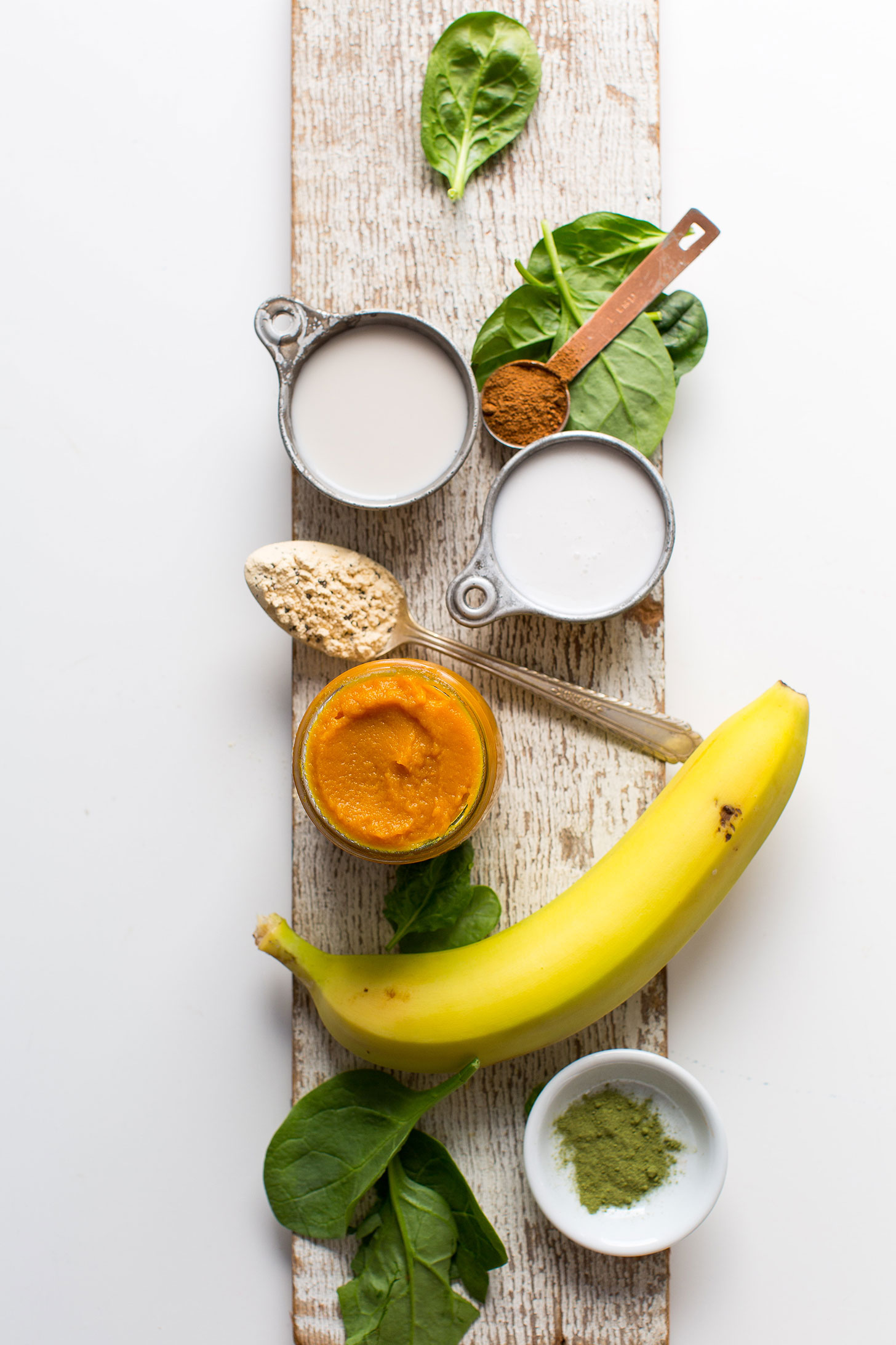 Wood plank with spinach, pumpkin pie spice, coconut milk, almond milk vegan vanilla protein powder, pumpkin puree, banana, and greens powder