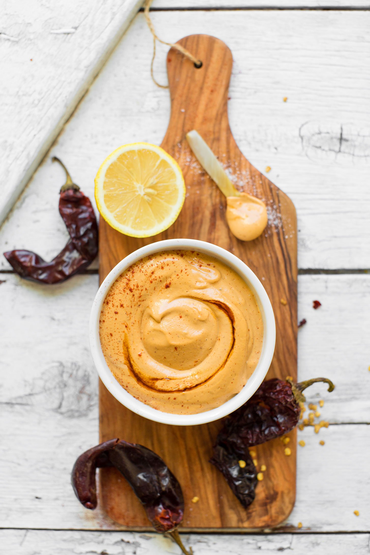 Wood cutting board with a bowl of creamy vegan chipotle aioli and ingredients used to make it