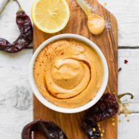 Bowl of Vegan Chipotle Aioli on a cutting board with chilies and lemon