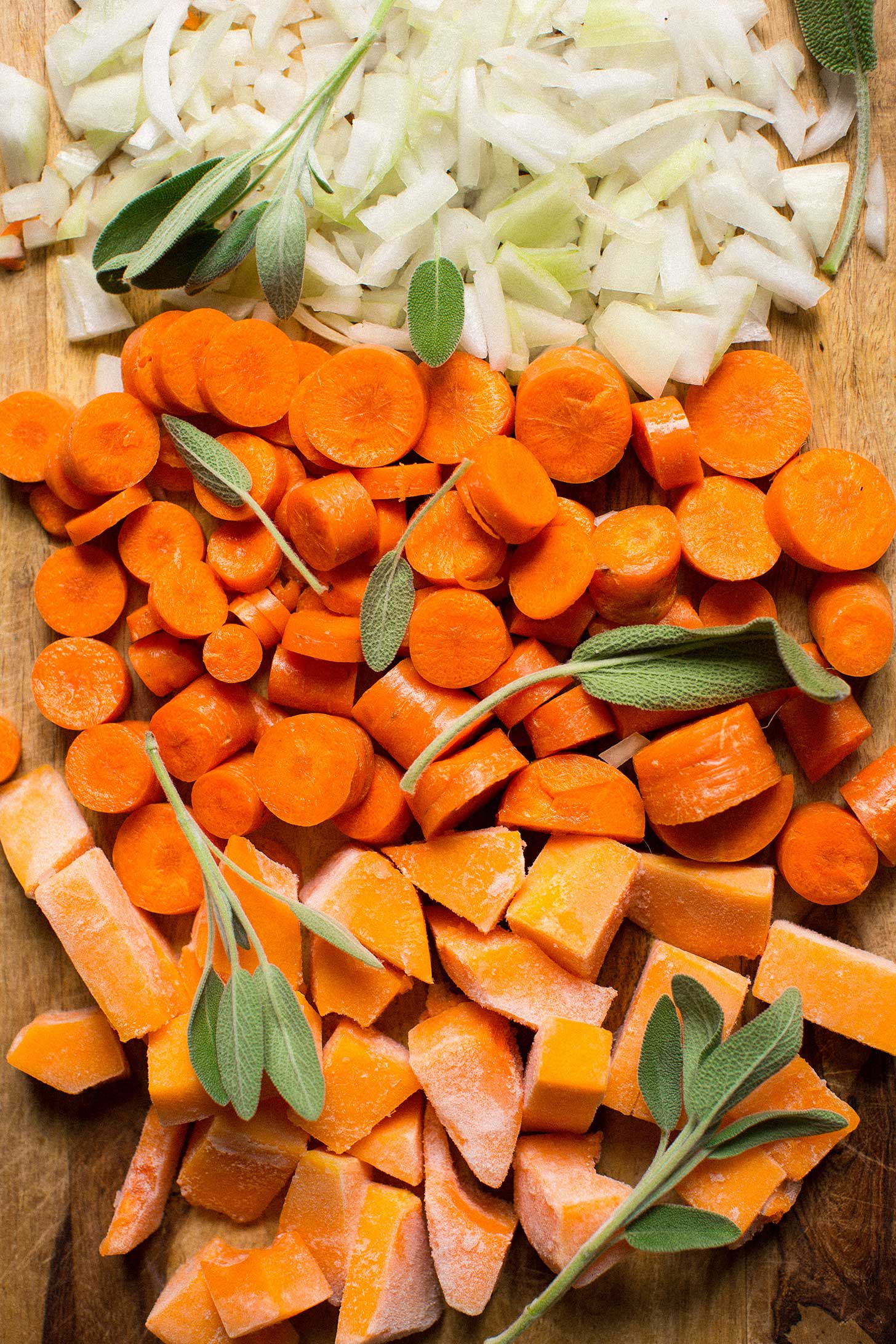 Cutting board with onions, carrots, butternut squash, and sage for making Acorn Squash soup
