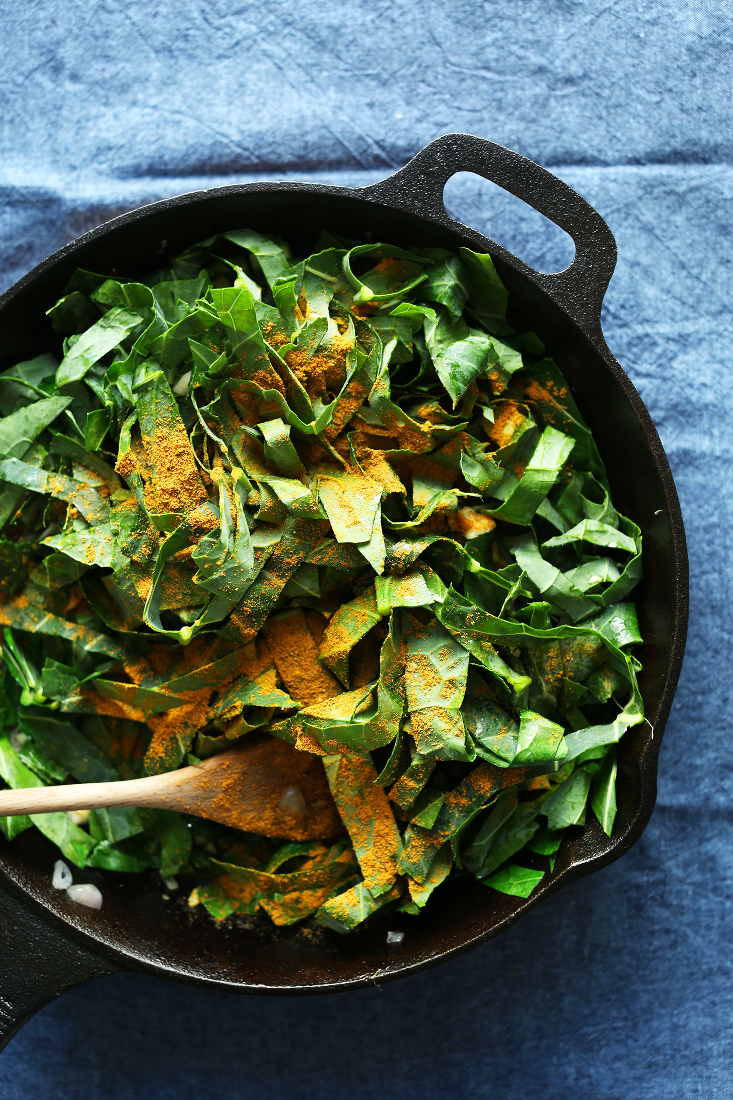 Collard greens and curry powder in a cast iron skillet ready to be made into a delicious vegan side dish