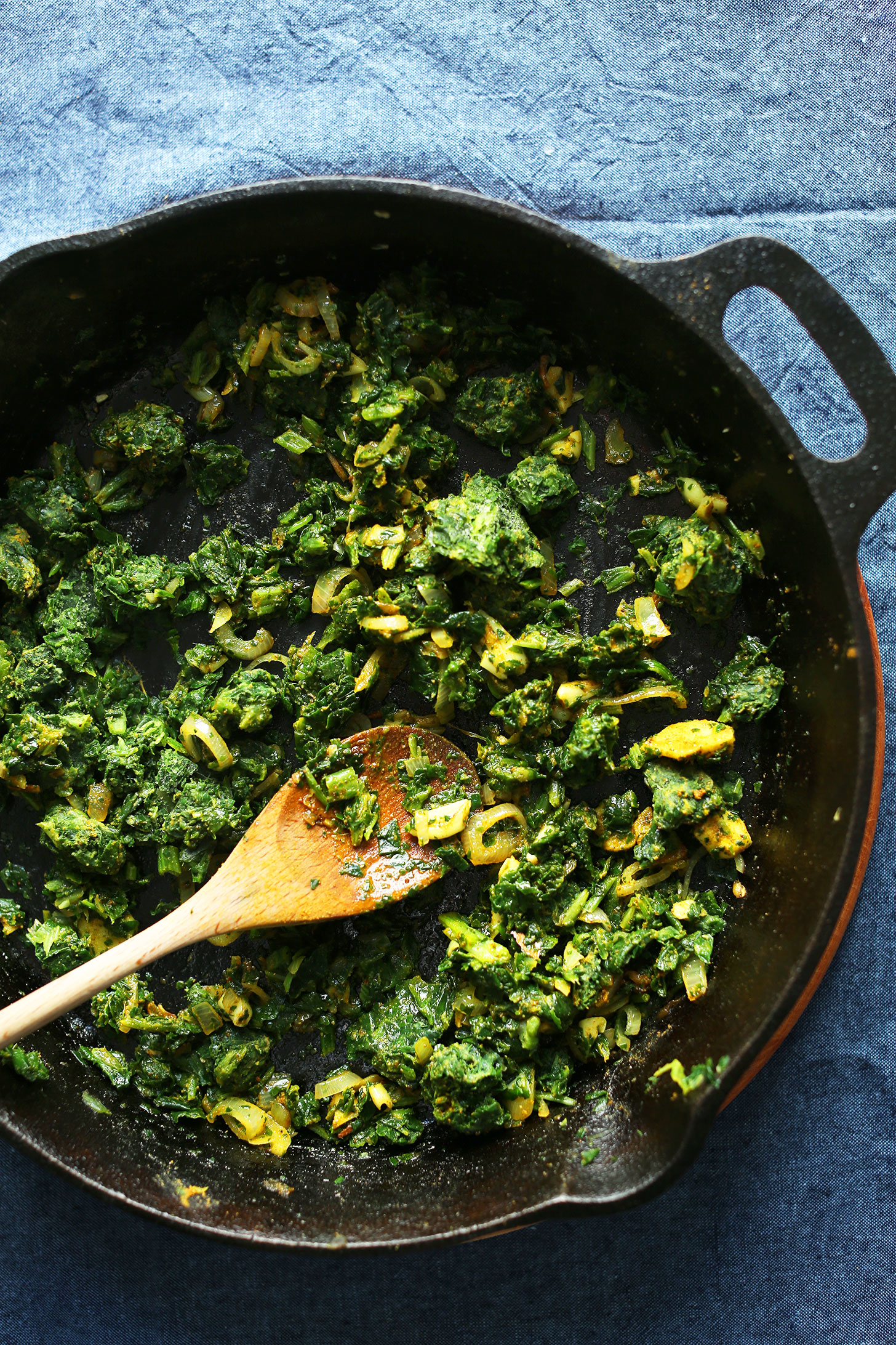 Stirring onions and greens in a cast iron pan for delicious Green Curry