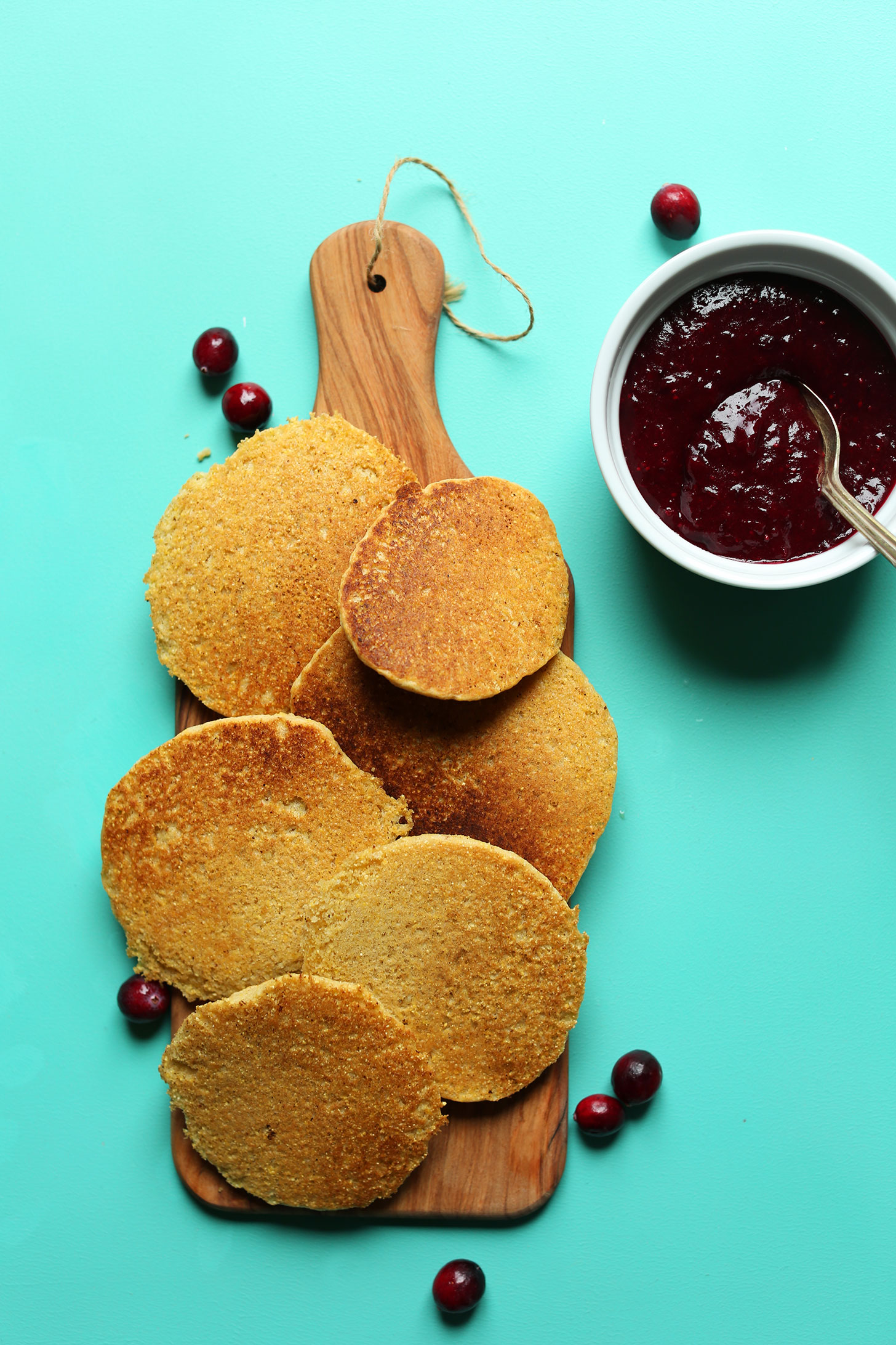 Wood cutting board with freshly made gluten-free cornmeal pancakes and a bowl of Cranberry Compote