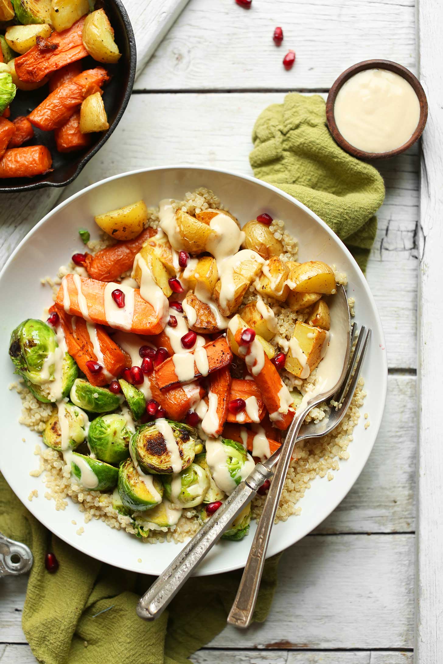 Dinner bowl filled with quinoa, roasted vegetables, tahini dressing, and pomegranate seeds