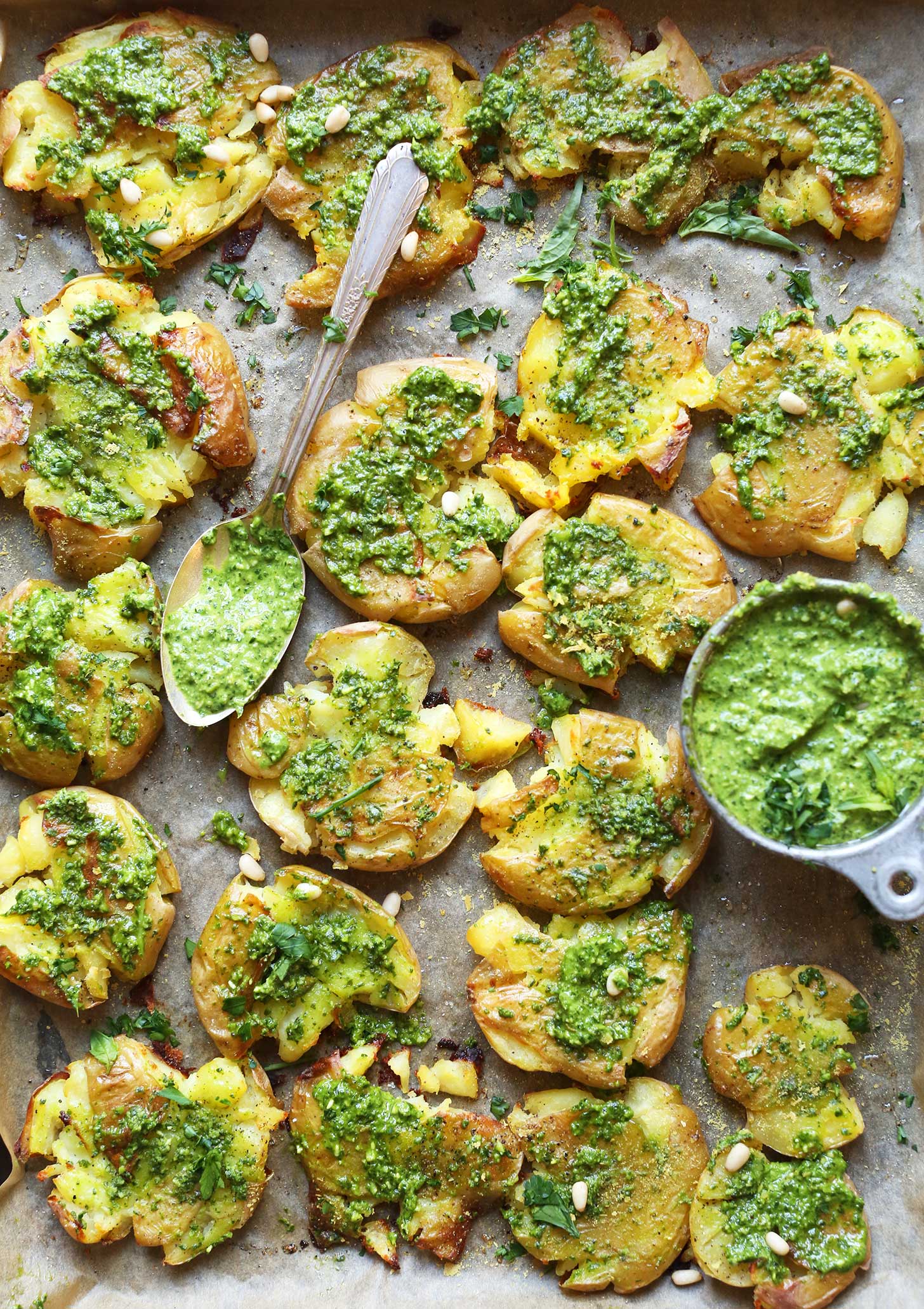 Parchment-lined baking sheet full of Smashed Potatoes smothered with vegan Garlic Herb Pesto