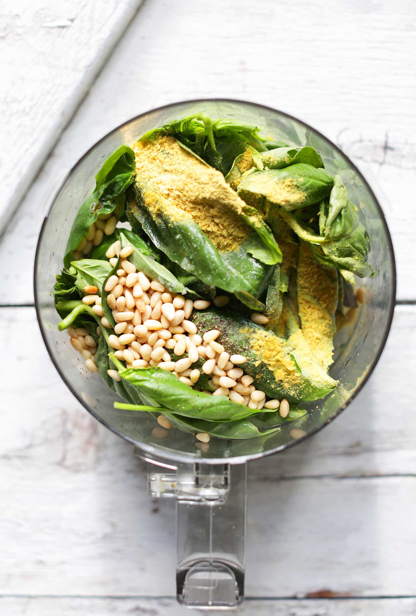Food processor with ingredients for vegan Garlic Herb Pesto