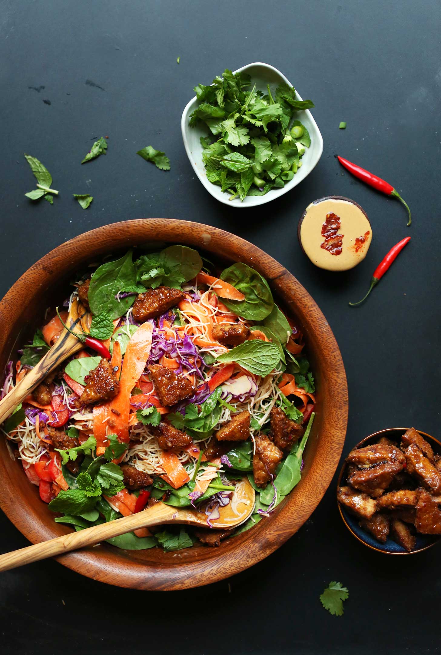 Using wooden spoons to grab a serving of Thai Salad with Marinated Peanut Tempeh for a healthy plant-based meal