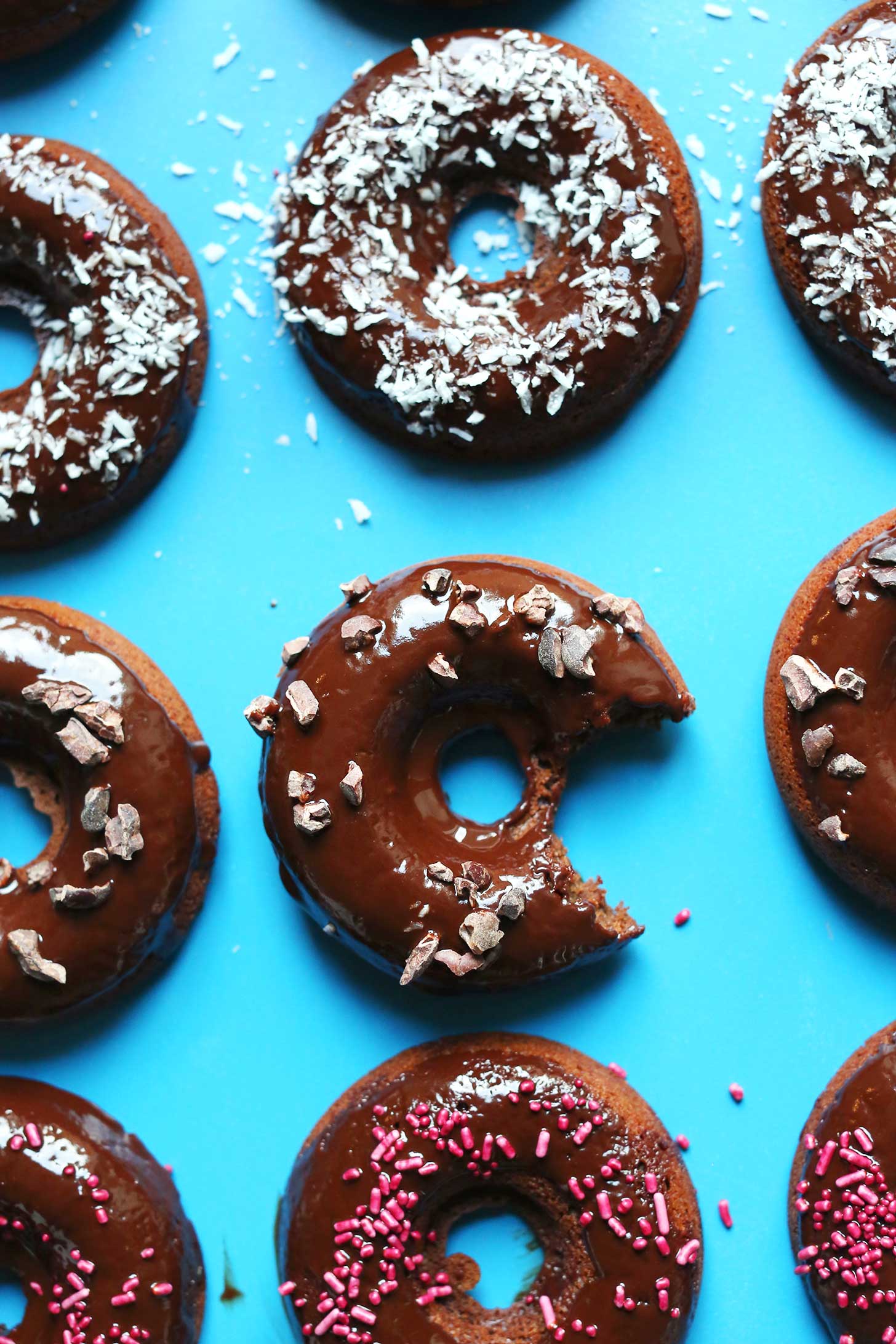 Glazed chocolate donuts topped with sprinkles, cacao nibs, or shredded coconut for a vegan gluten-free dessert