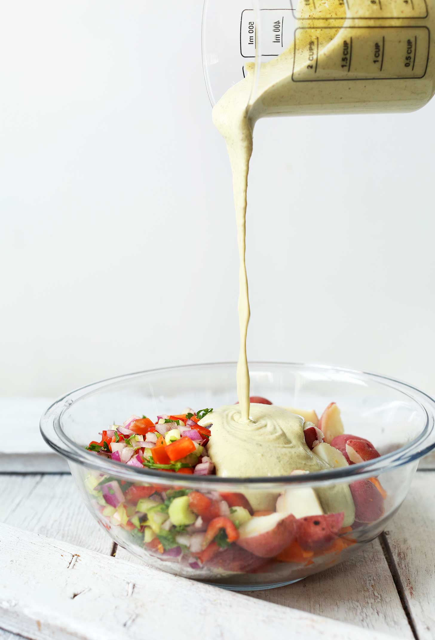 Pouring dressing onto a bowl of our Simple Vegan Potato Salad recipe