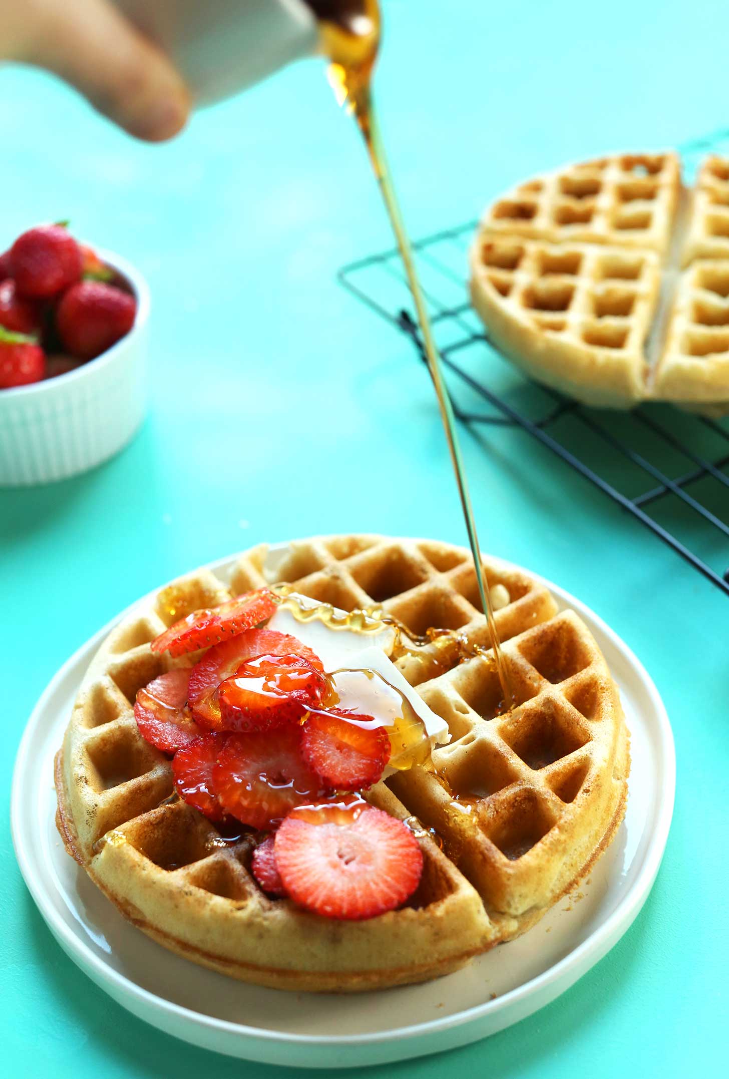 Pouring syrup onto gluten-free vegan waffles that are crispy on the outside and fluffy on the inside