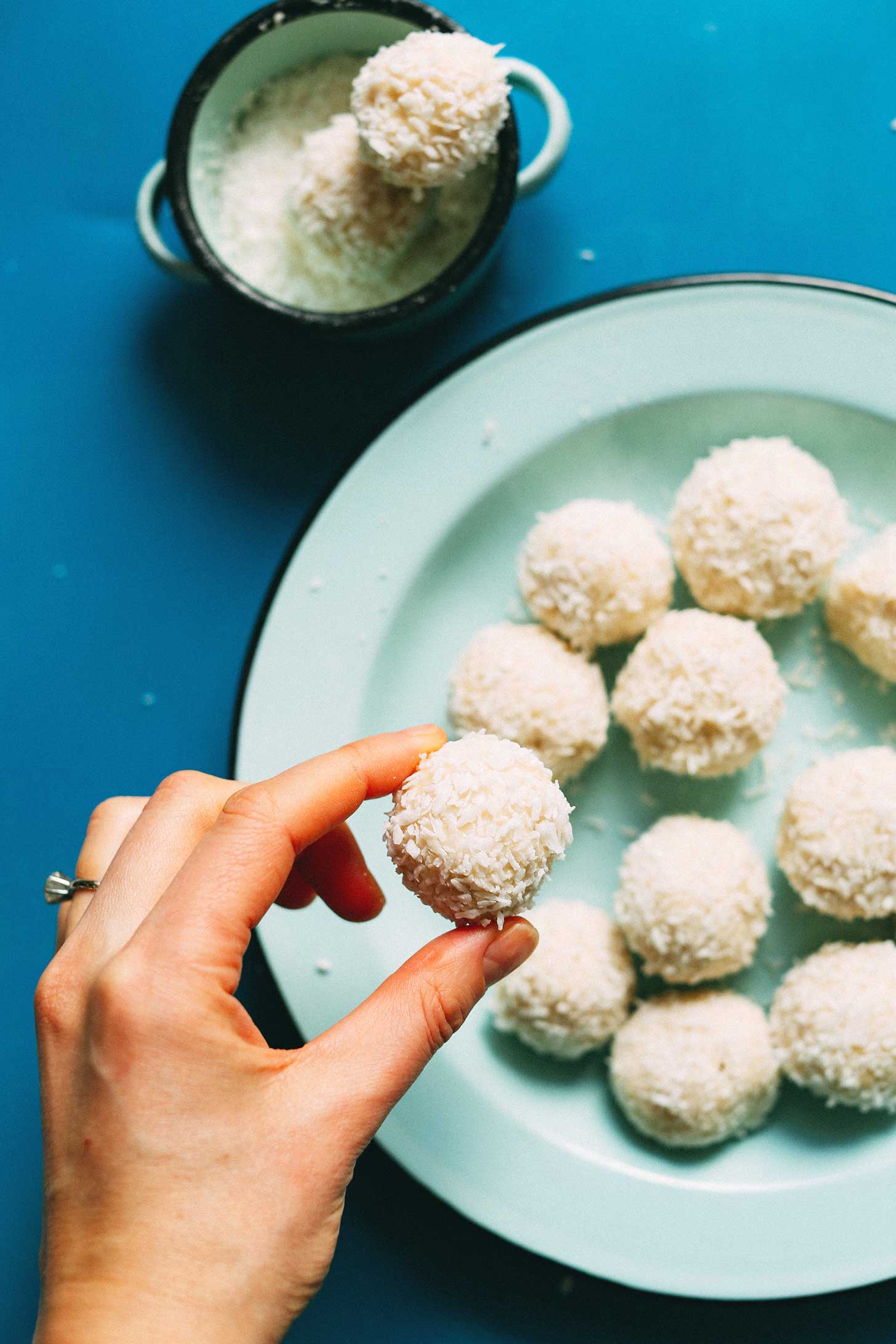 Picking up a truffle off a plate full of Vegan White Chocolate Truffles