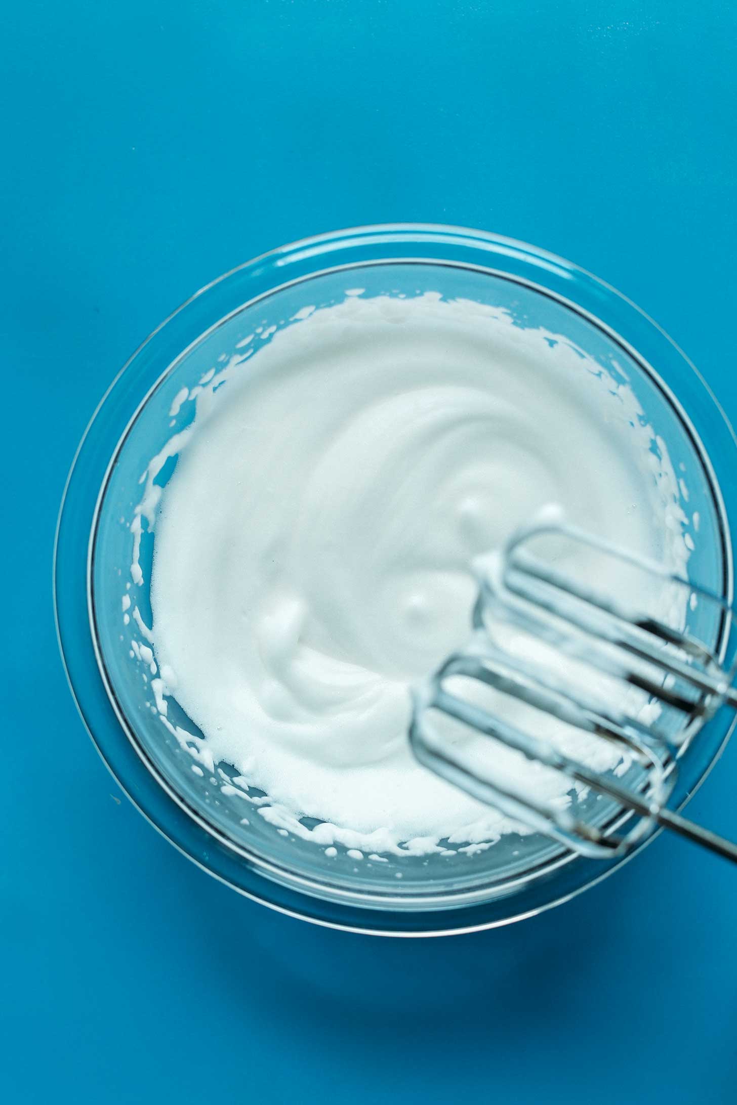 Electric mixer blades over a bowl of freshly whipped aquafaba
