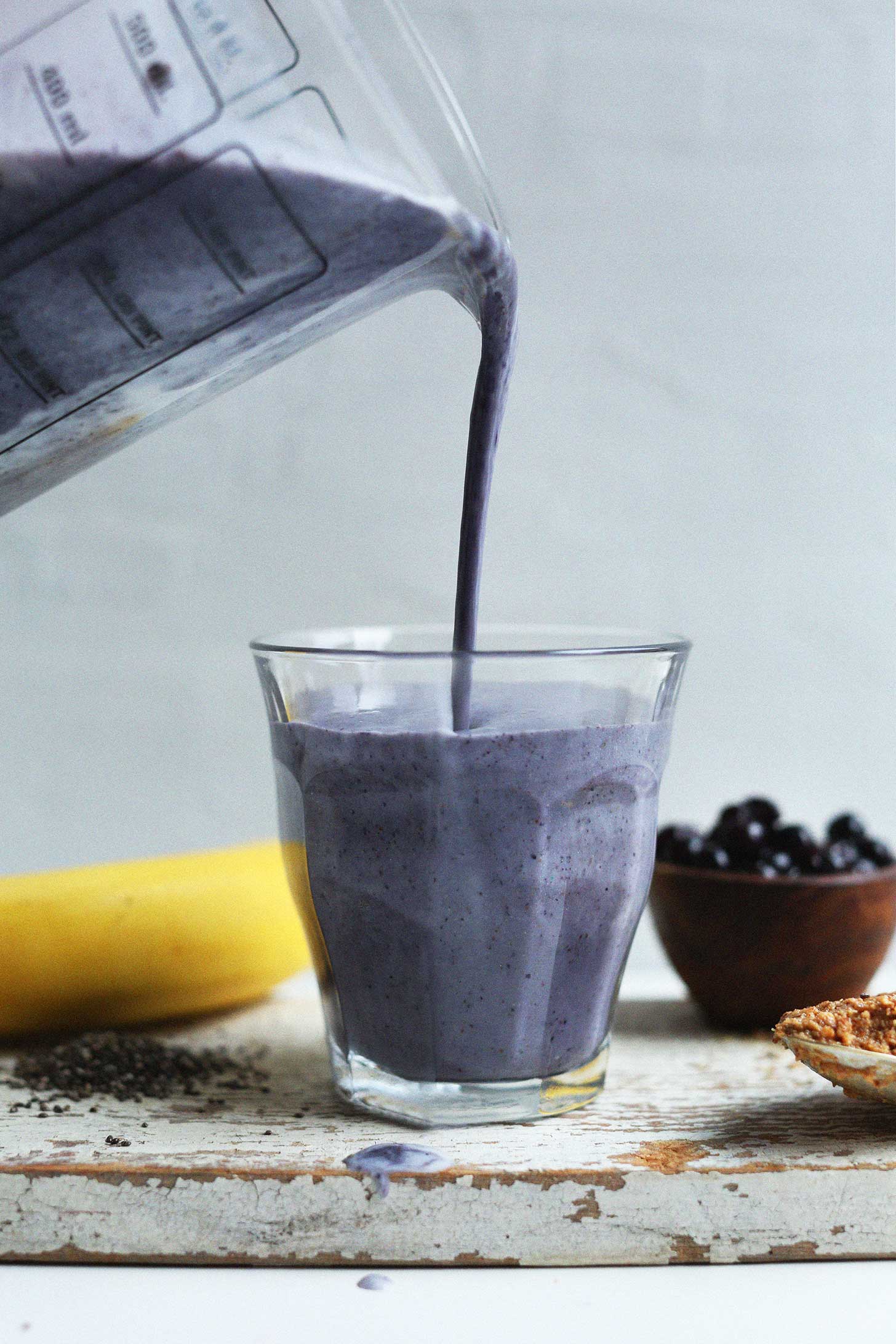 Pouring Almond Butter Blueberry Smoothie into a glass for a plant-based breakfast