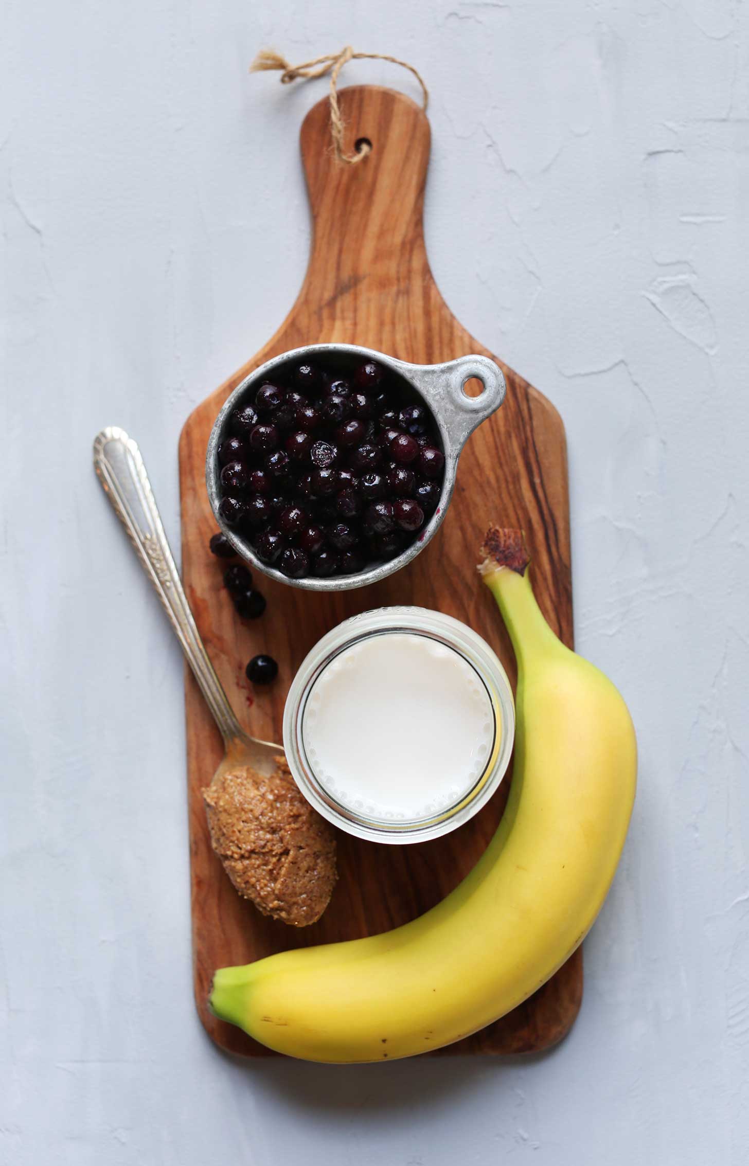 Wood board with blueberries, almond milk, almond butter, and banana for making a delicious vegan smoothie recipe