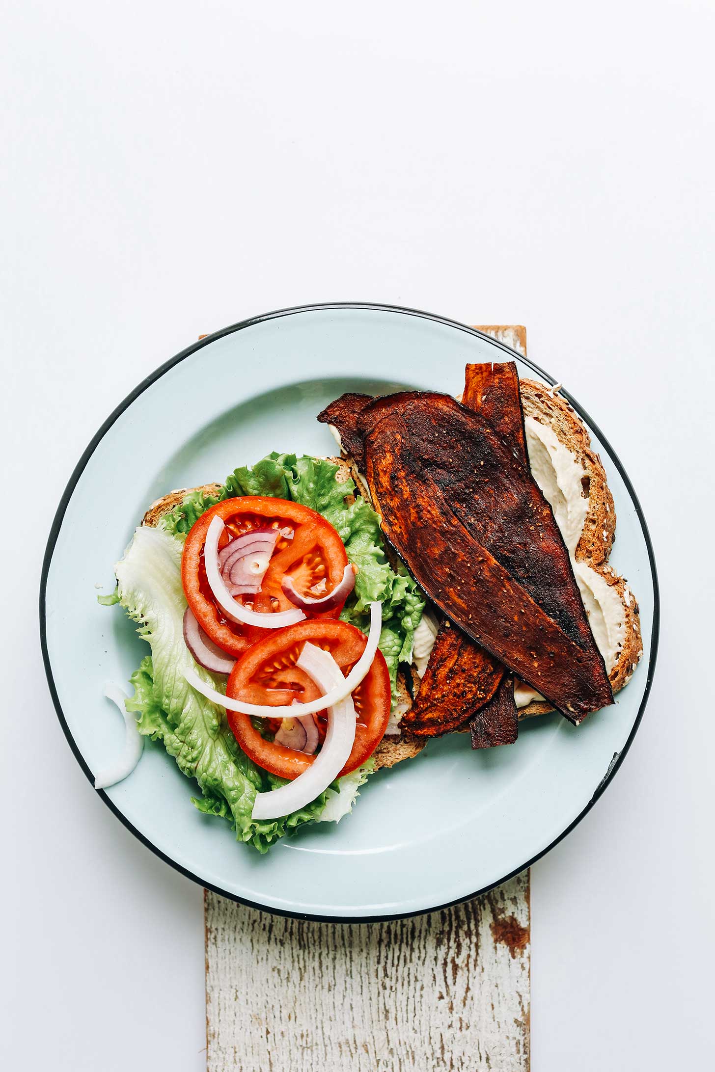 A plate with eggplant bacon, oil-free vegan mayo, sliced tomato, onion, and lettuce for a Vegan BLT