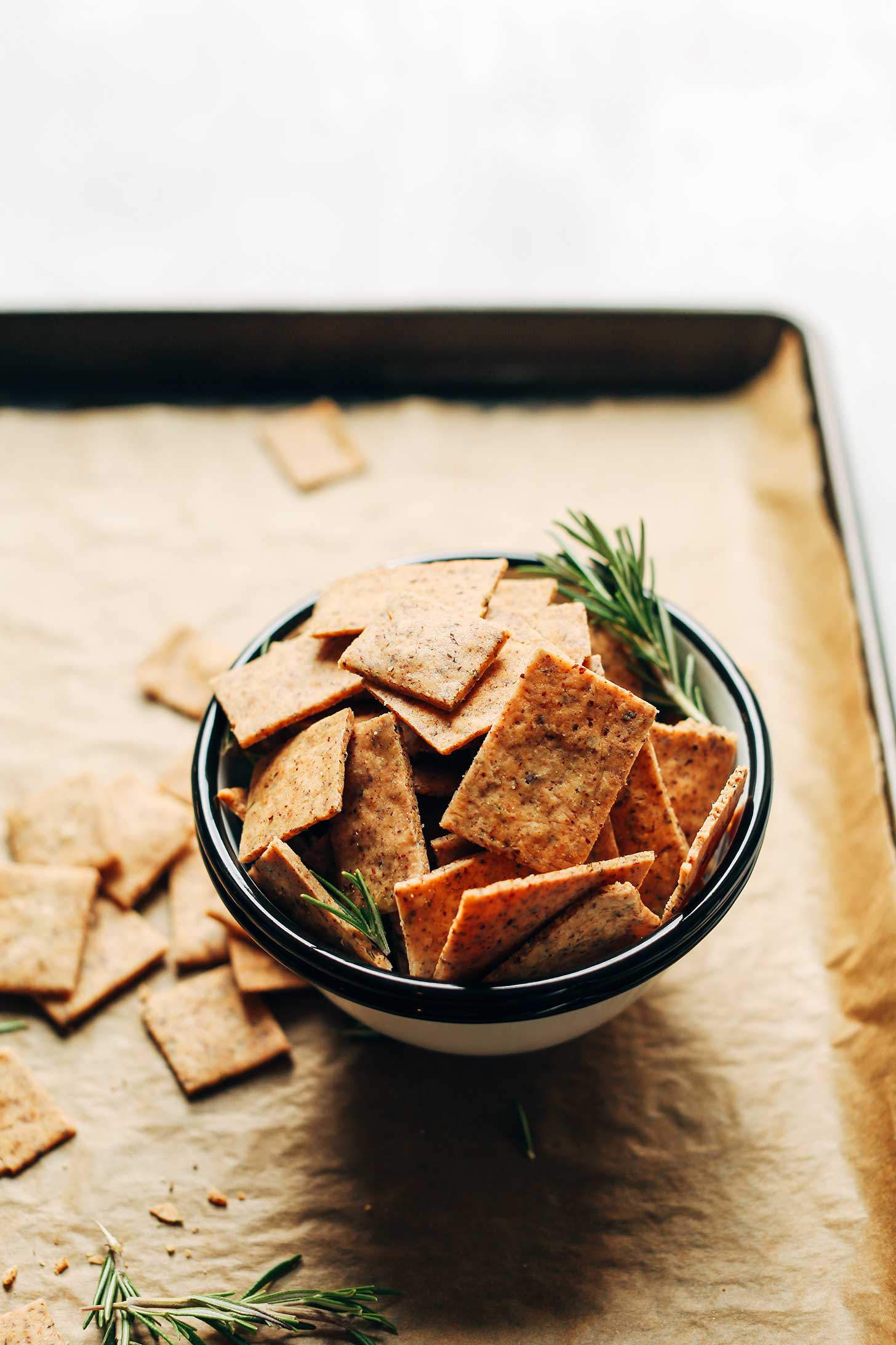 Close up shot of a bowl of Vegan Gluten-Free Crackers on a parchment-lined baking sheet