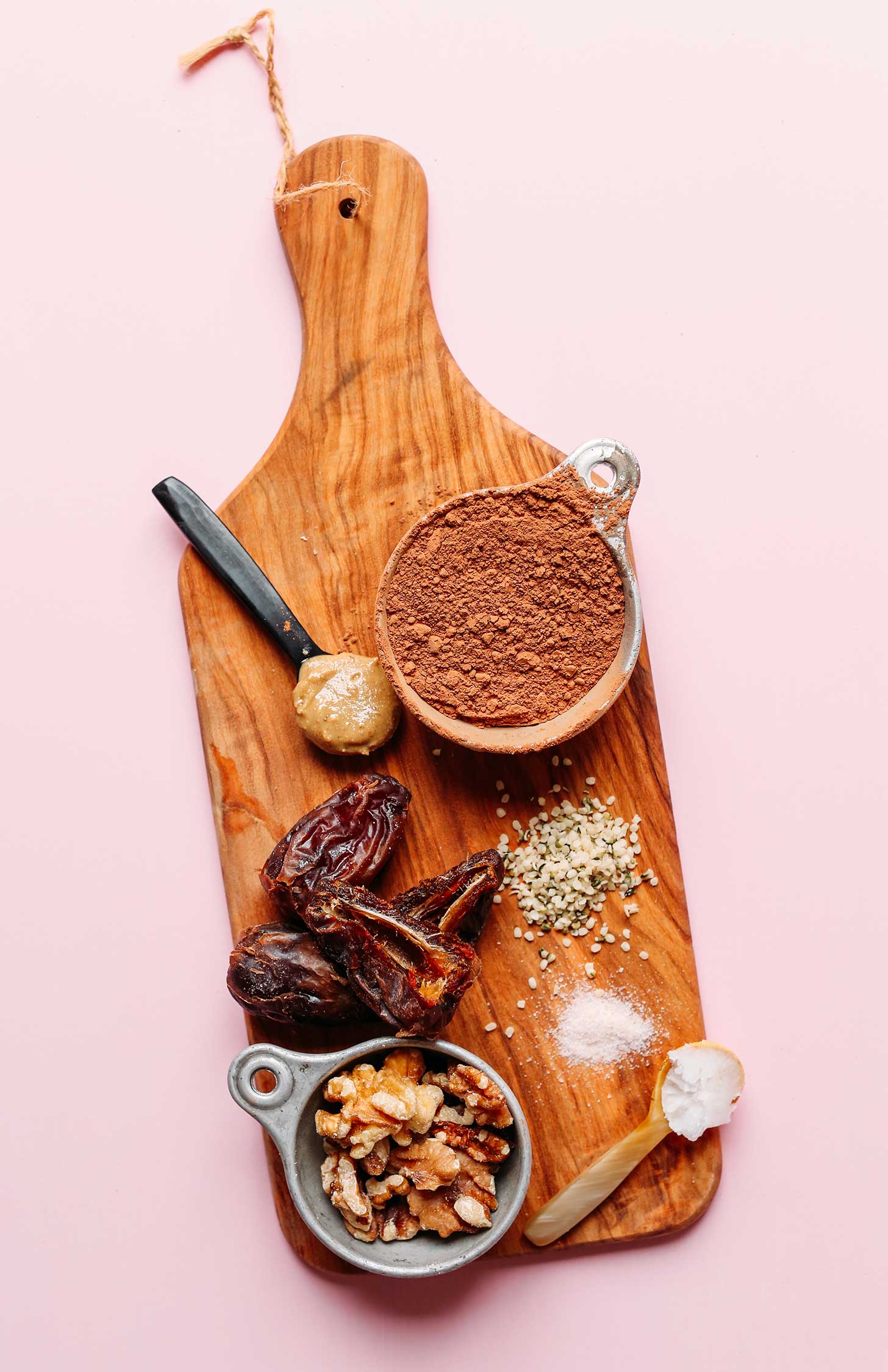 Wood board with walnuts, dates, nut butter, cacao powder, hemp seeds, salt, and coconut oil for making Chocolate Hemp Energy Bites