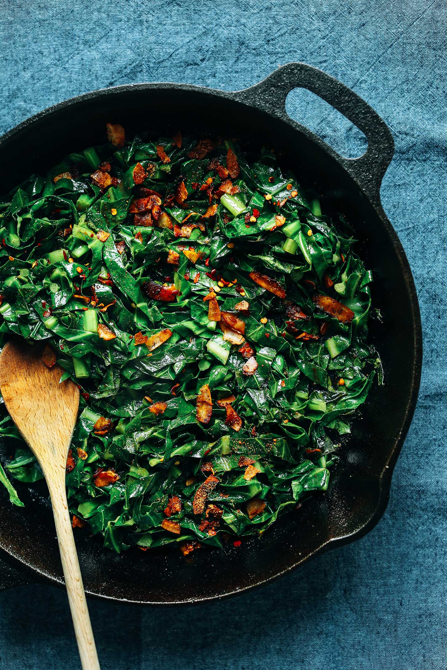 Using a wooden spoon to stir Collard Greens with Coconut Bacon in a cast iron skillet