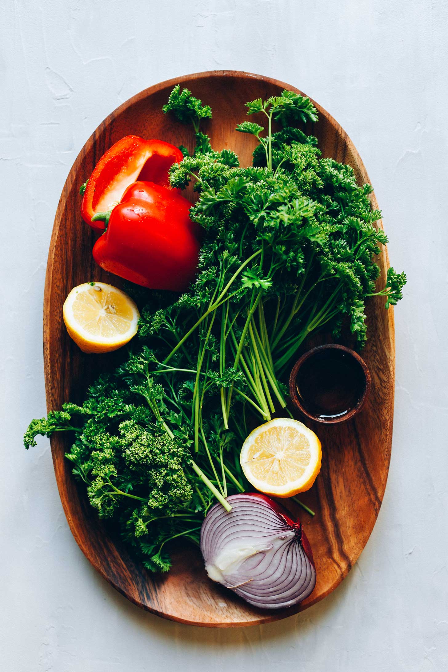 Wood serving platter with red bell pepper, curly parsley, lemon, onion, and olive oil for making Grain-Free Tabbouleh Salad