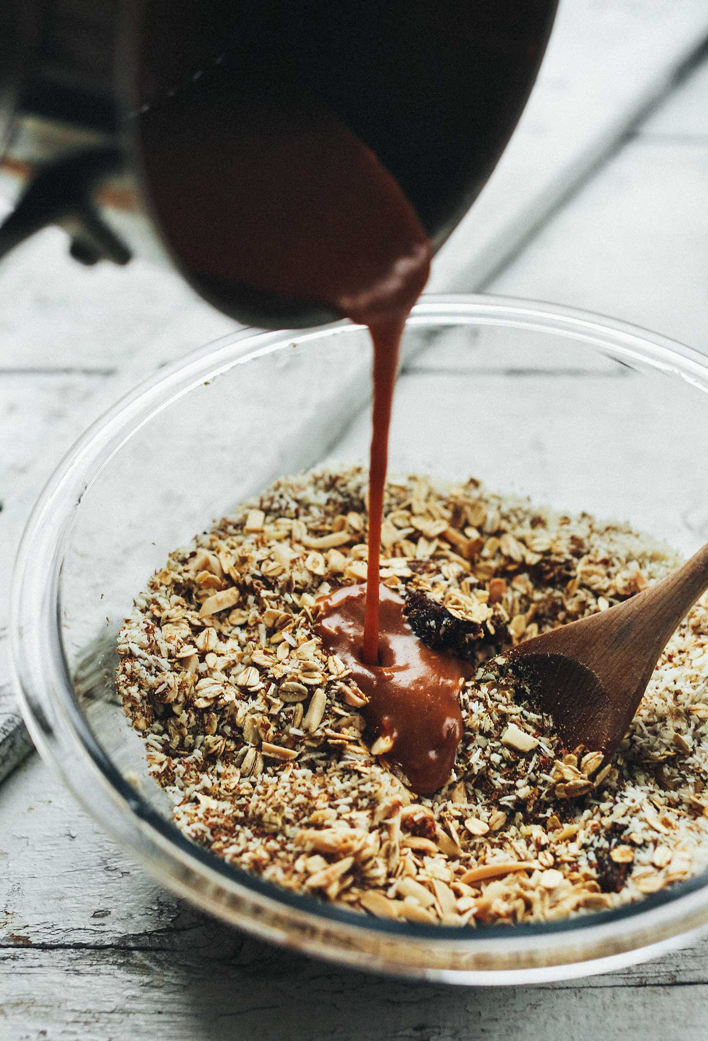 Pouring almond butter, coconut oil, syrup mixture into oat mixture