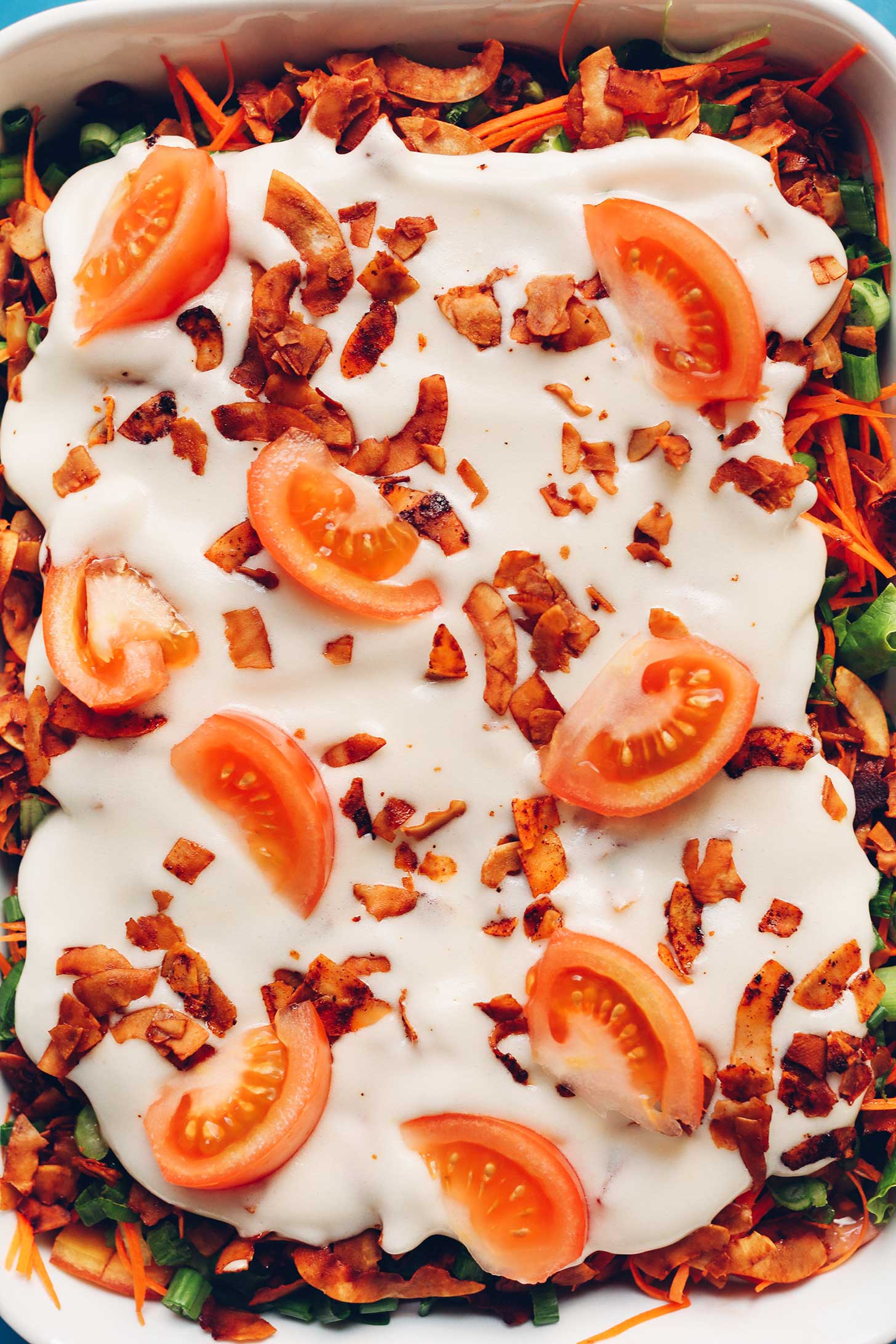 Ceramic dish full of Vegan 7-Layer Salad with a mayo, coconut bacon, and tomato top