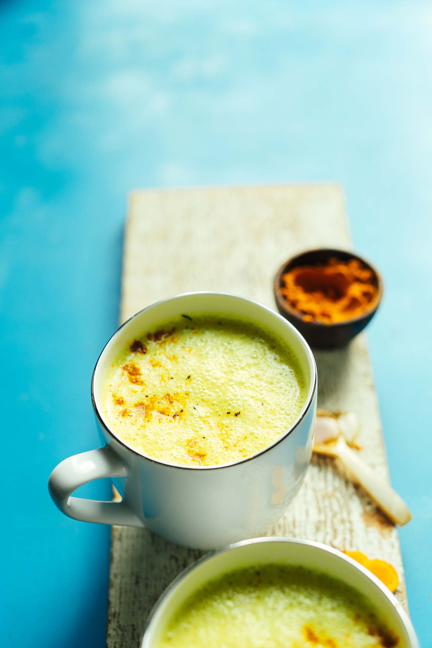 Wood plank with a mug of Creamy Vegan Golden Milk and turmeric