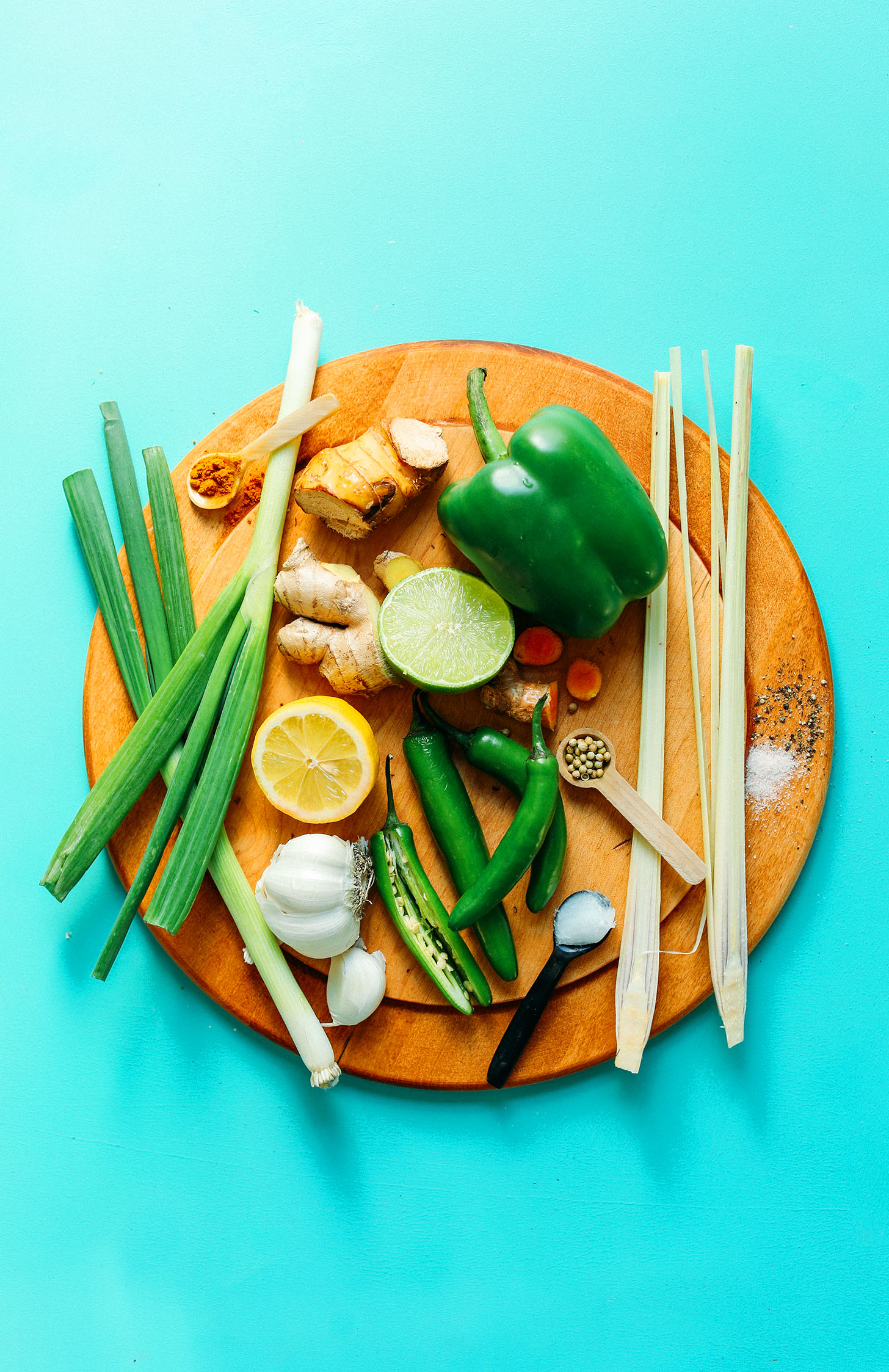 Wood cutting board with lemongrass, green bell pepper, lime, turmeric, galangal, ginger, lemon, serranos, garlic, green onion, salt, and spices for homemade easy green curry paste