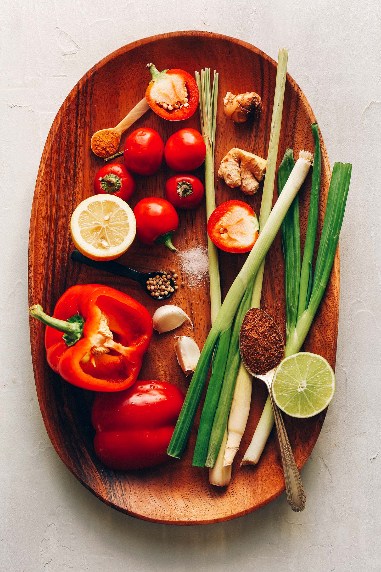 Wood tray with red bell pepper, chilies, lemongrass, green onion, lemon, lime, garlic, and spices