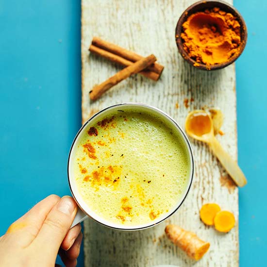 Wood platter with a mug of vegan Golden Milk alongside ingredients to make it