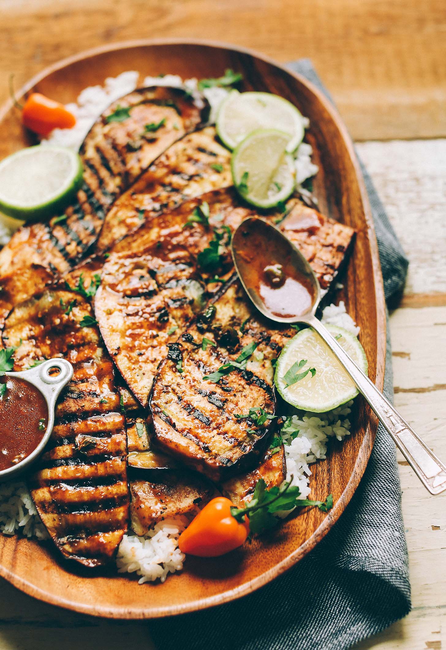 A wood platter with Grilled Vegan Jamaican Jerk Eggplant over rice with lime wedges