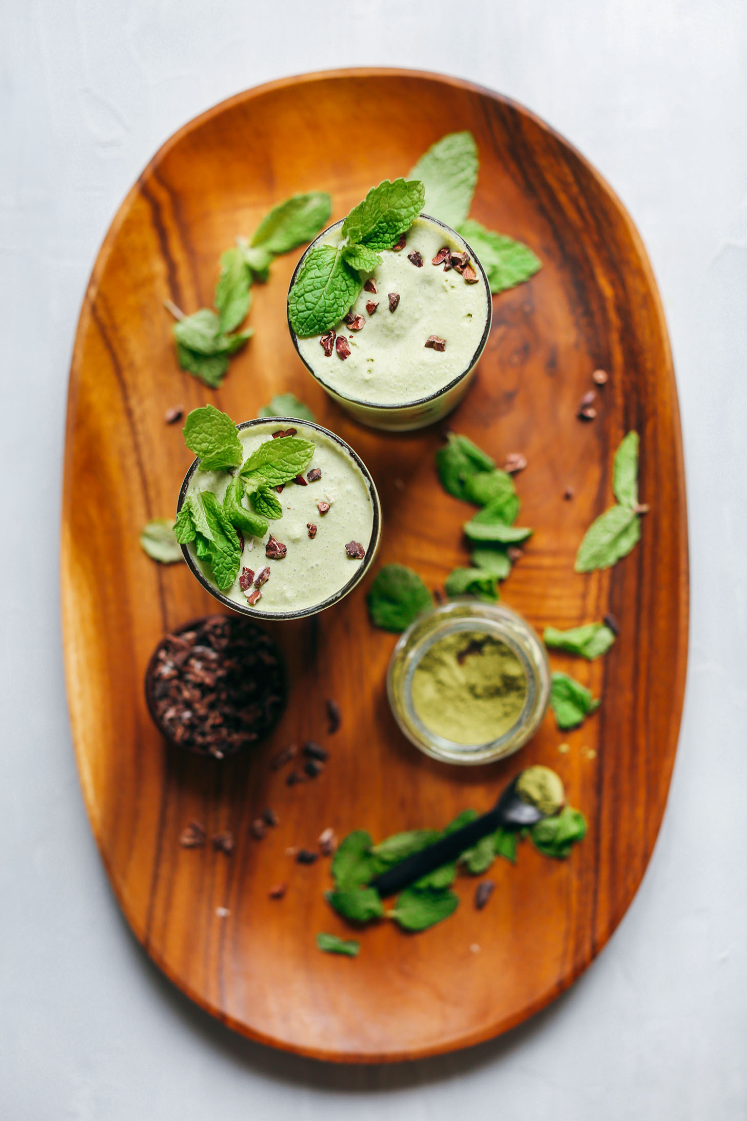 Wood platter with cacao nibs, matcha, and two glasses of our Vegan Mint Matcha Shake