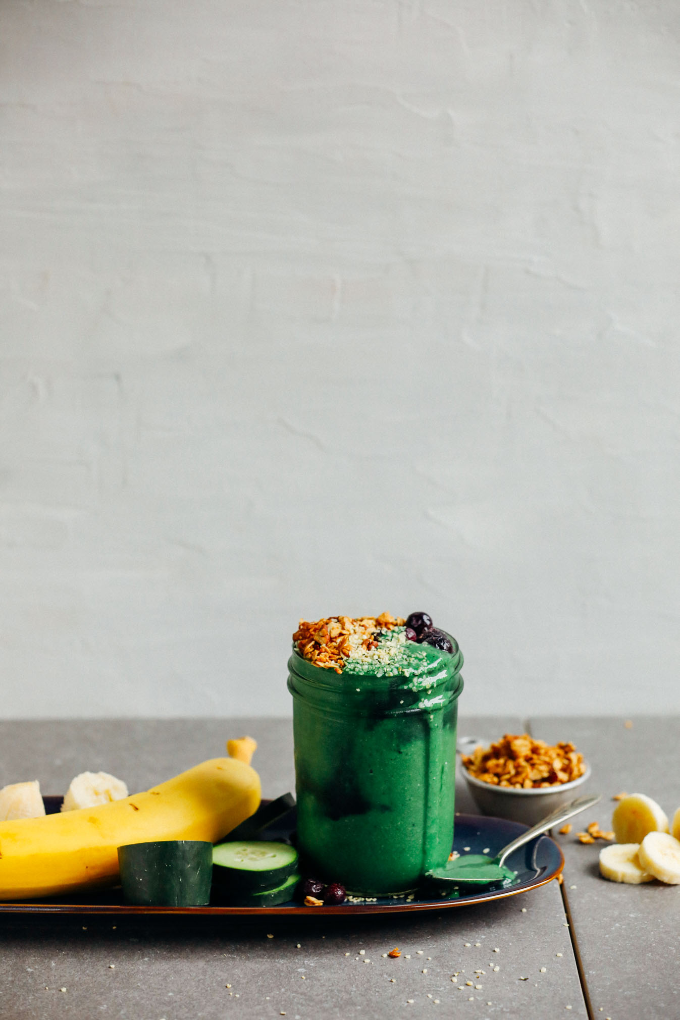 Platter with a jar of Super Green Smoothie with Spirulina and fresh fruits and vegetables used to make it