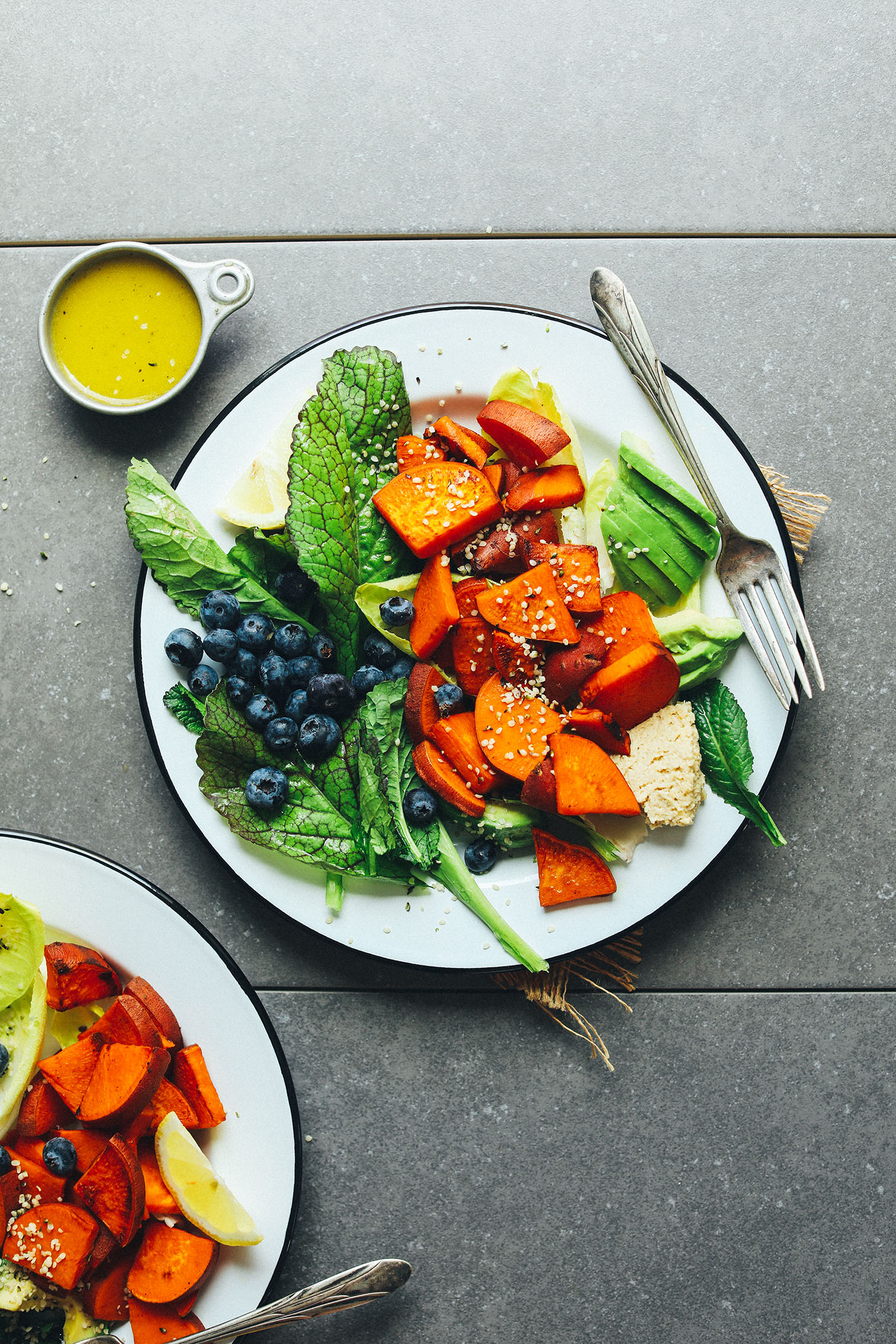 Plate of nourishing Vegan Breakfast Salad with hummus, blueberries, avocado, sweet potato, greens, and dressing