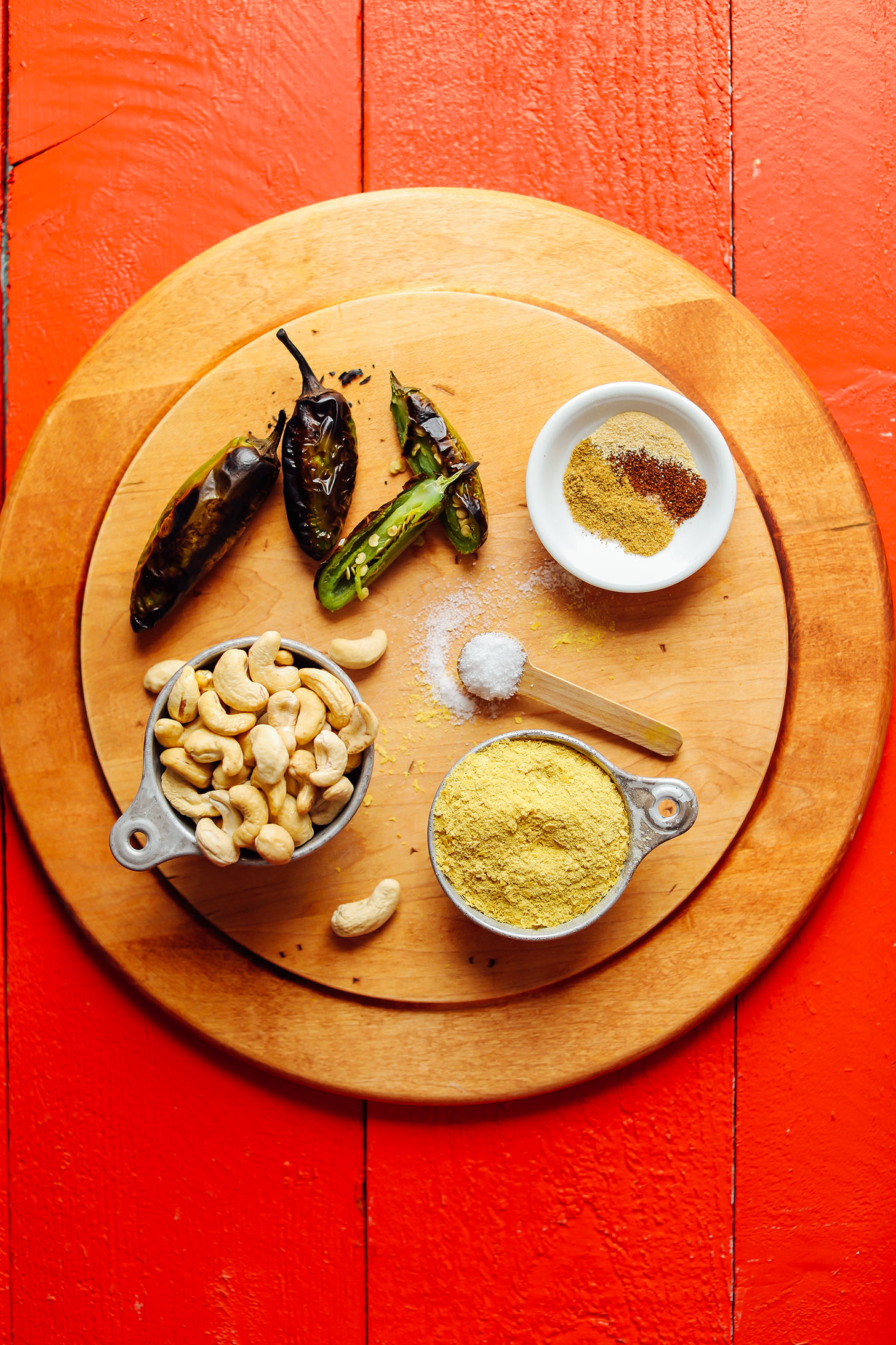 Wood cutting board with roasted jalapenos, cashews, nutritional yeast, salt, and spices for Creamy Roasted Jalapeno Vegan Queso