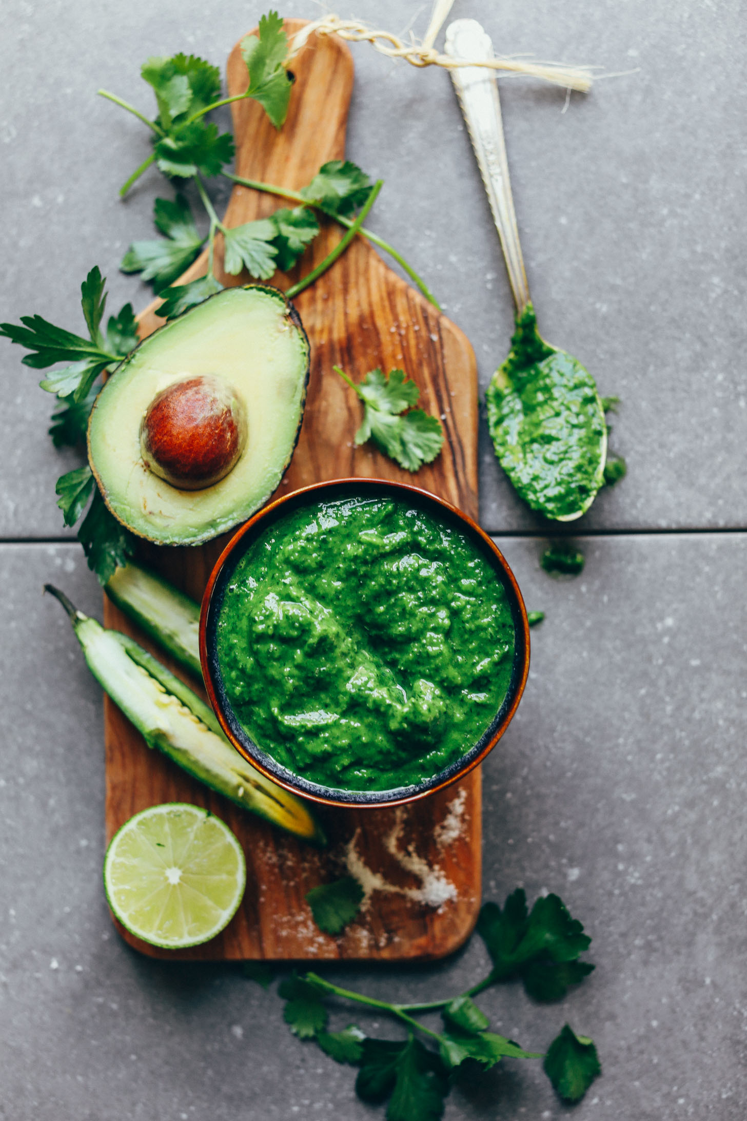 Wood cutting board with a bowl of homemade vegan Chimichurri sauce and fresh ingredients used to make it