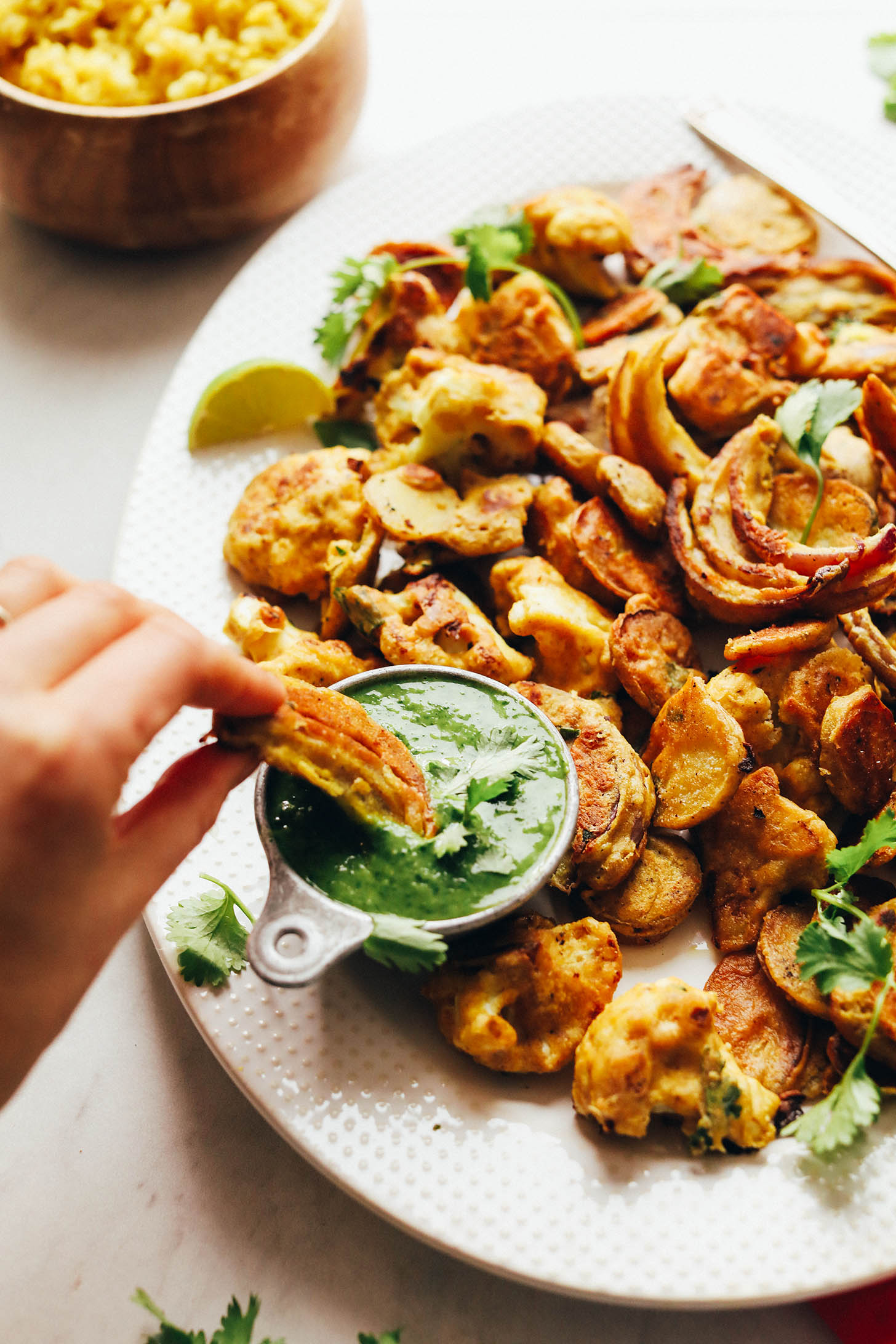 Dipping gluten-free Vegetable Pakoras into a measuring cup filled with flavorful green chutney