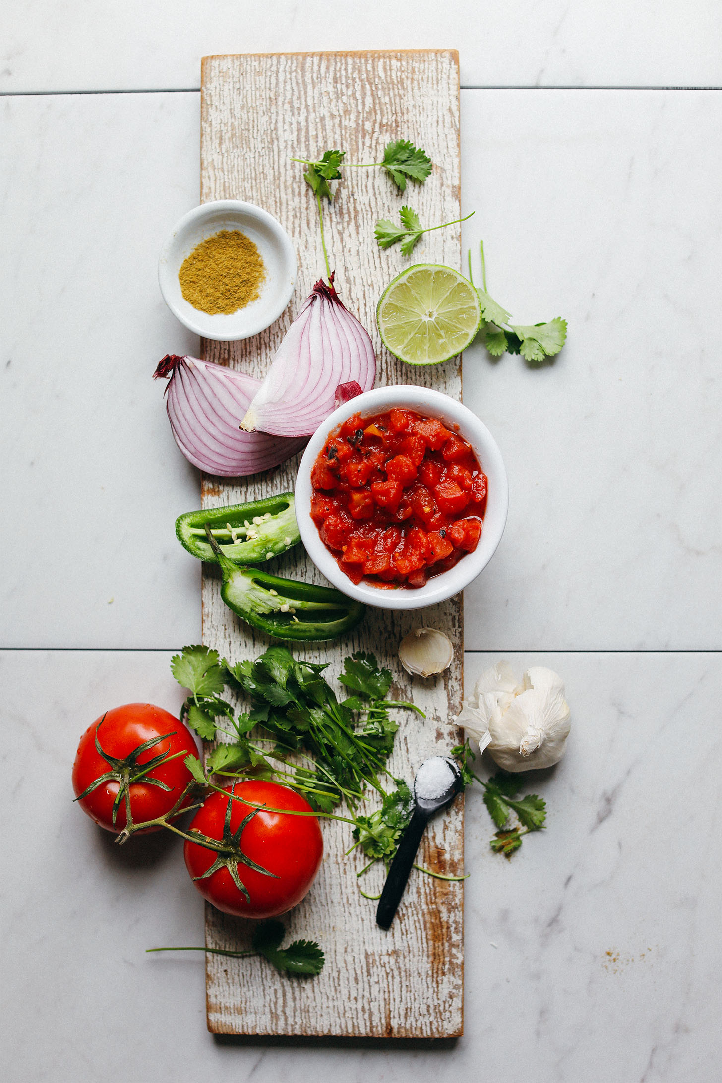 Wood plank with tomatoes, cilantro, garlic, jalapenos, red onion, lime, and cumin for making healthy homemade Red Salsa