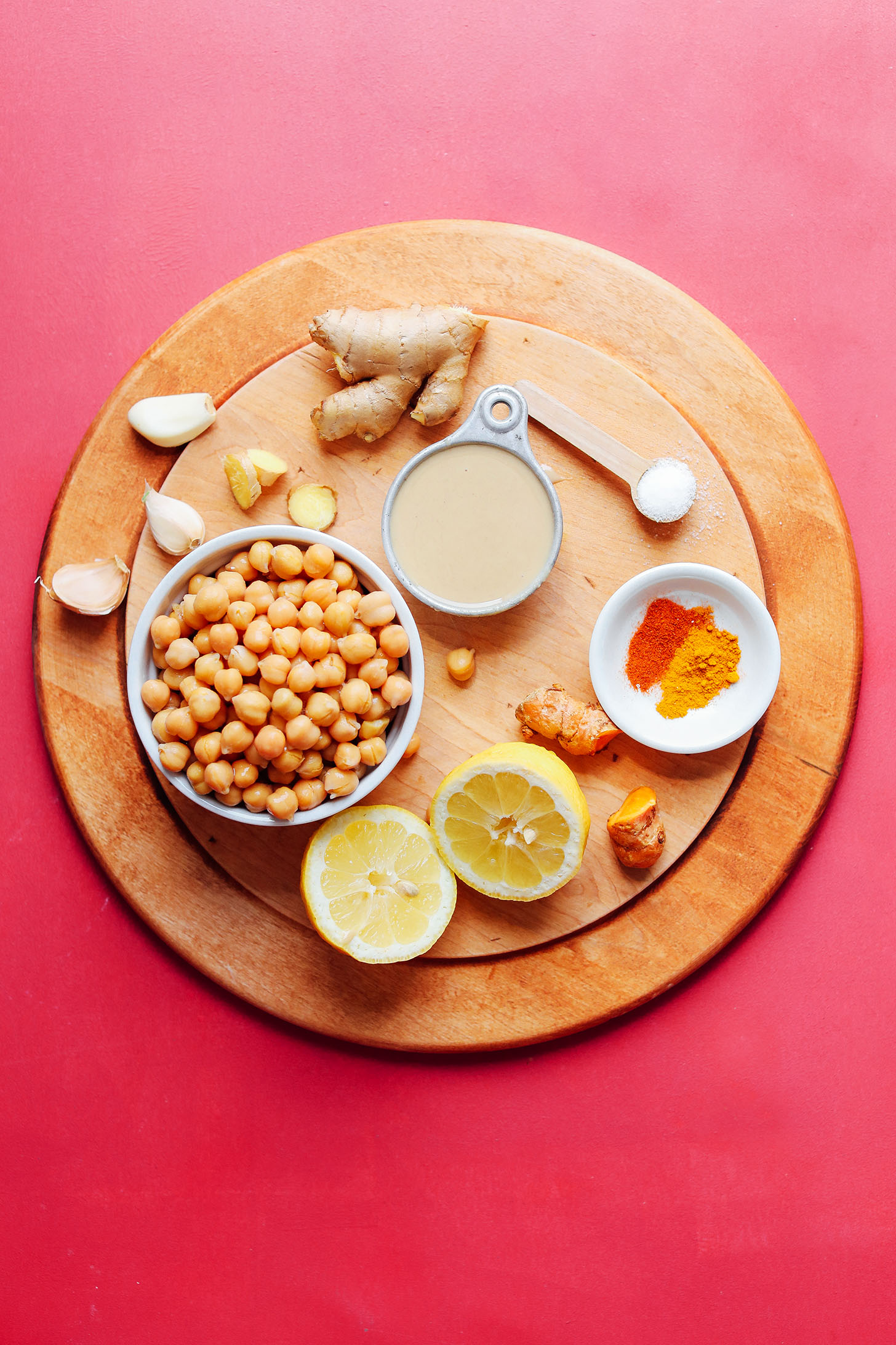 Wood cutting board with chickpeas, garlic, ginger, lemon, salt, and spices for making Golden Goddess Hummus