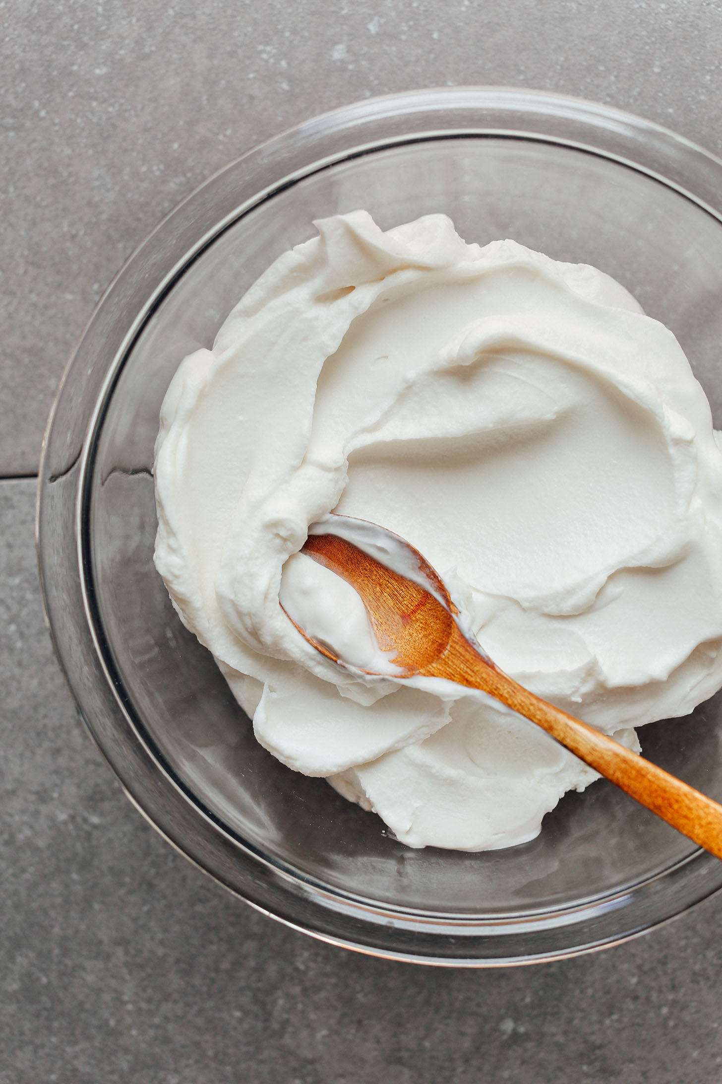 Stirring coconut yogurt with a wooden spoon in a glass mixing bowl