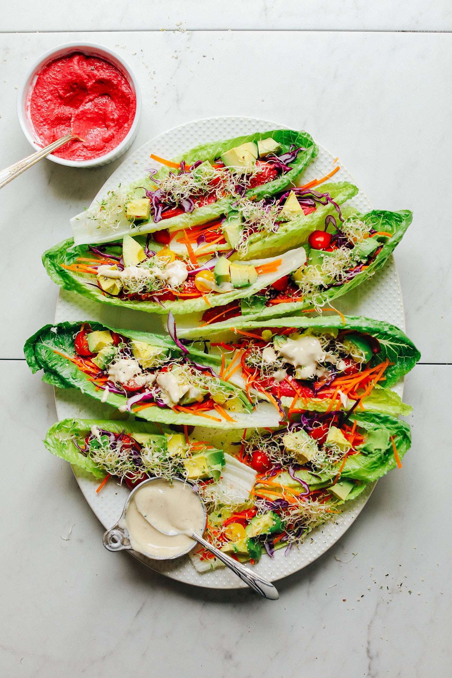Platter full of Romaine Taco Boats filled with fresh veggies, beet hummus, and tahini dressing