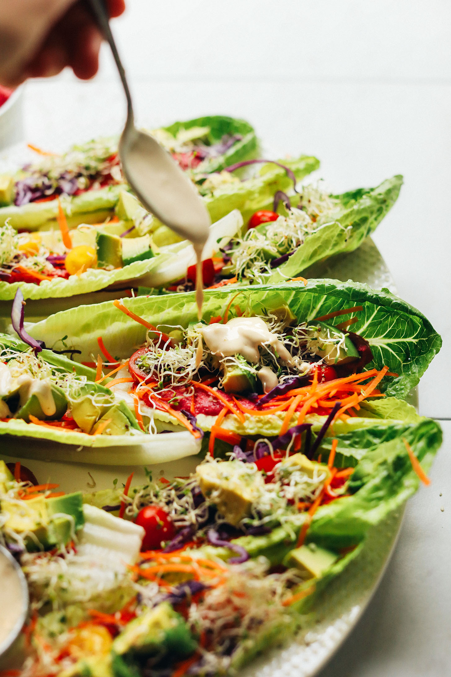 Drizzling tahini dressing onto Raw Romaine Taco Boats for a refreshing vegan meal