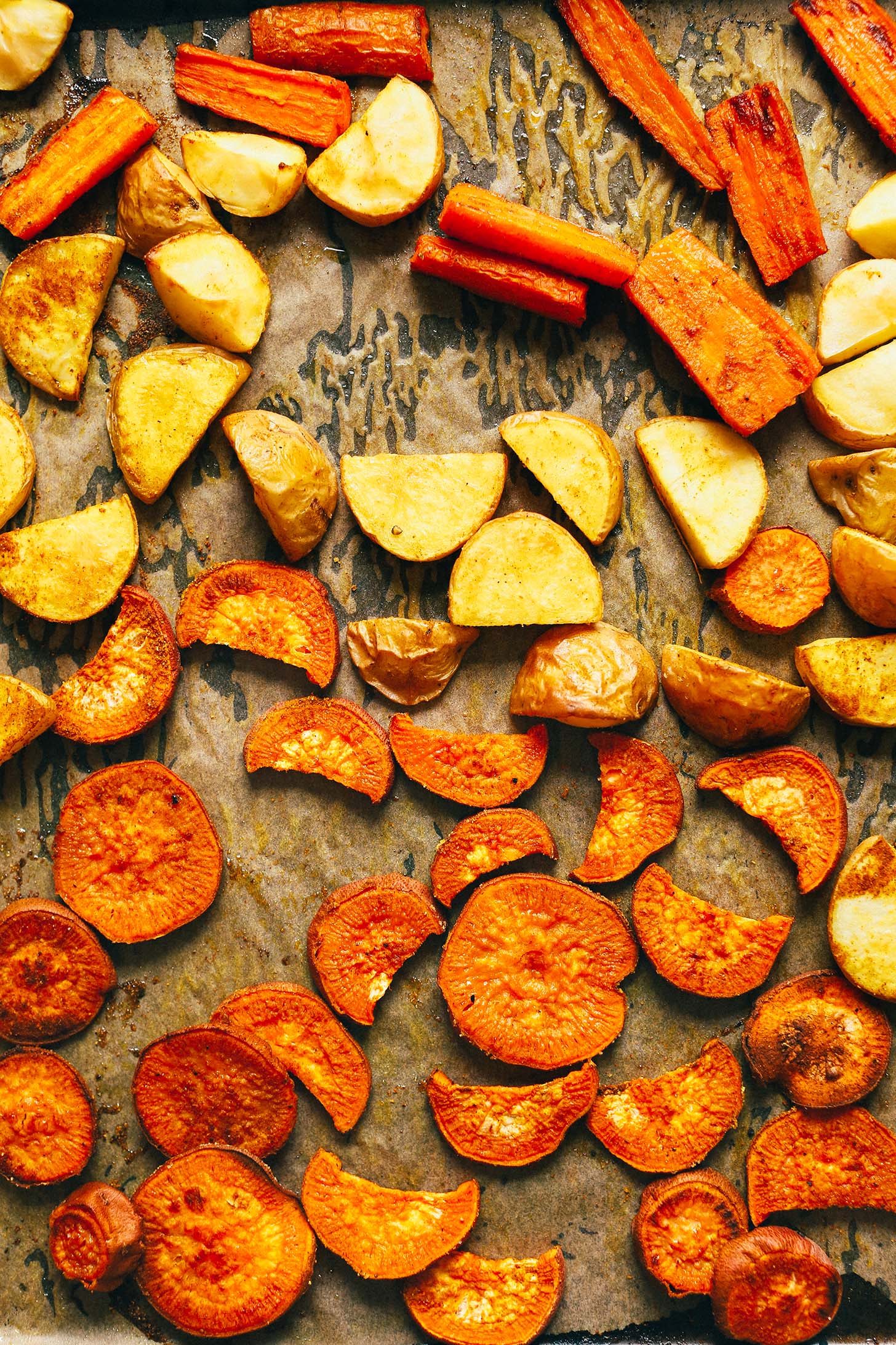 Parchment-lined baking sheet with sweet potato, carrot, and potato for making Roasted Vegetable Salad