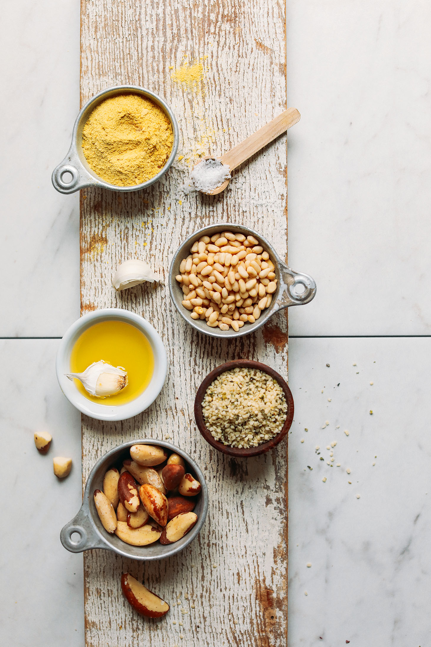 Wooden plank with nutritional yeast, pine nuts, garlic, olive oil, hemp seeds, and brazil nuts for making Vegan Parmesan Cheese