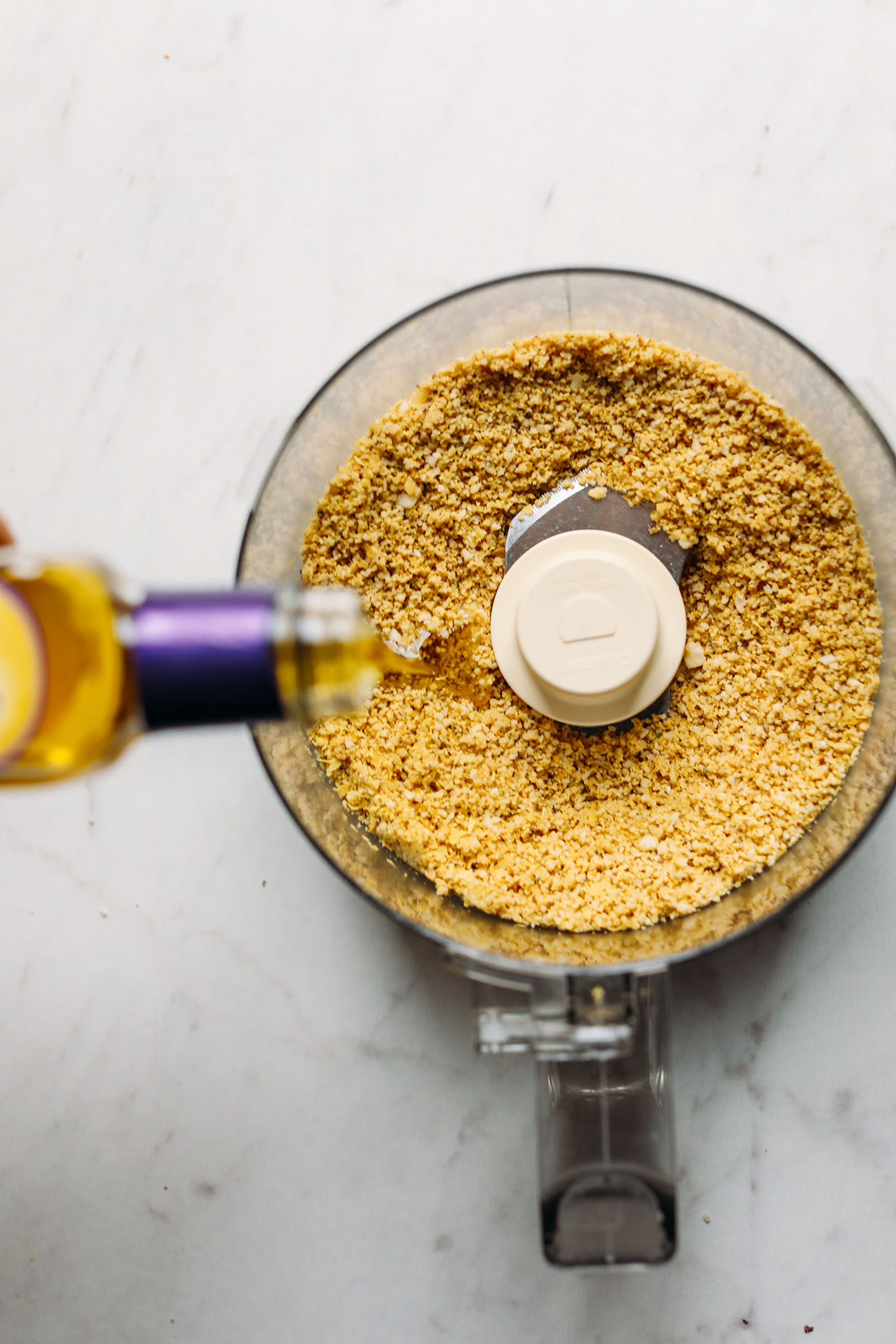 Pouring a bit of olive oil into the food processor for Vegan Parmesan Cheese