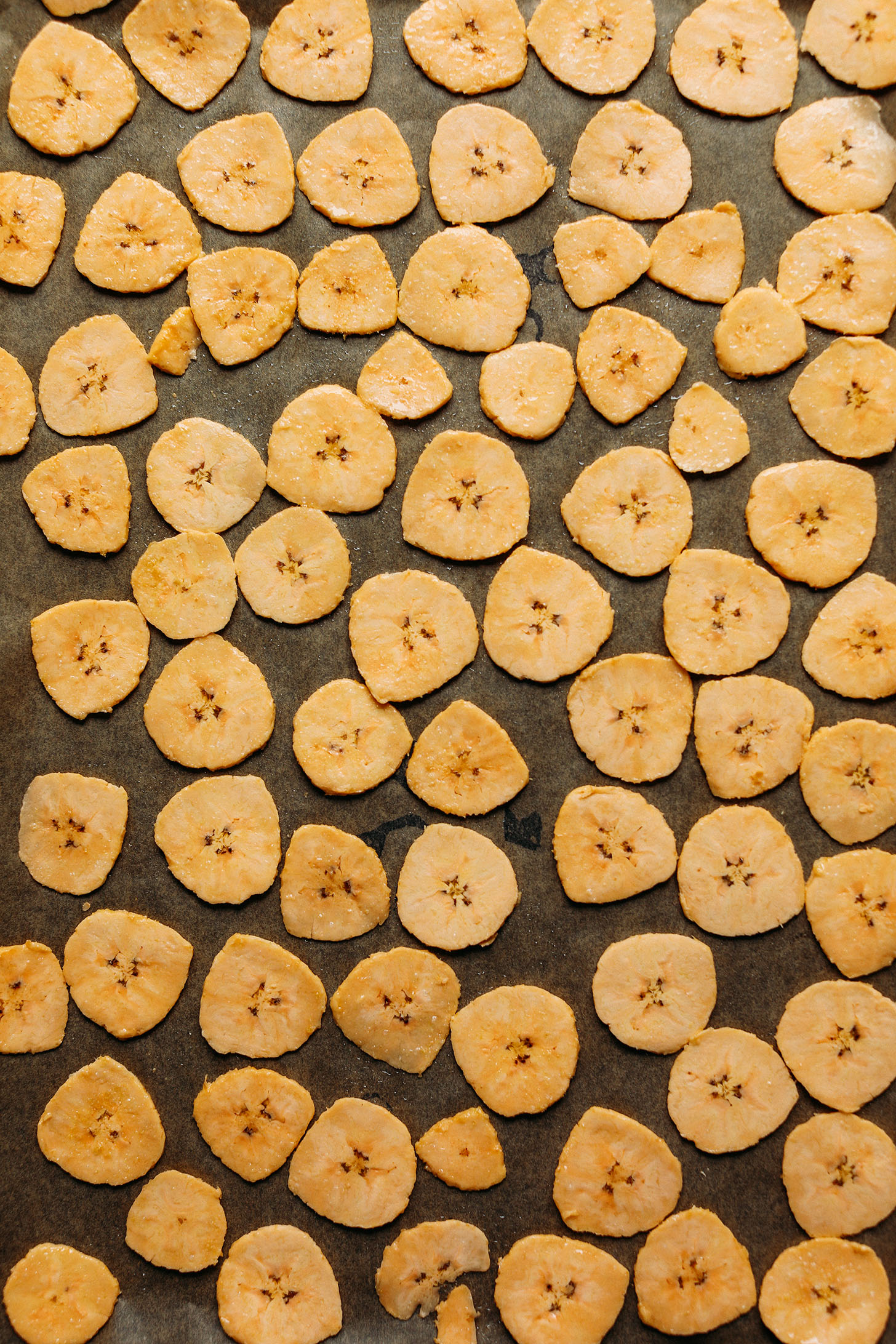 Sliced and seasoned plantain chips in a single layer on a baking sheet