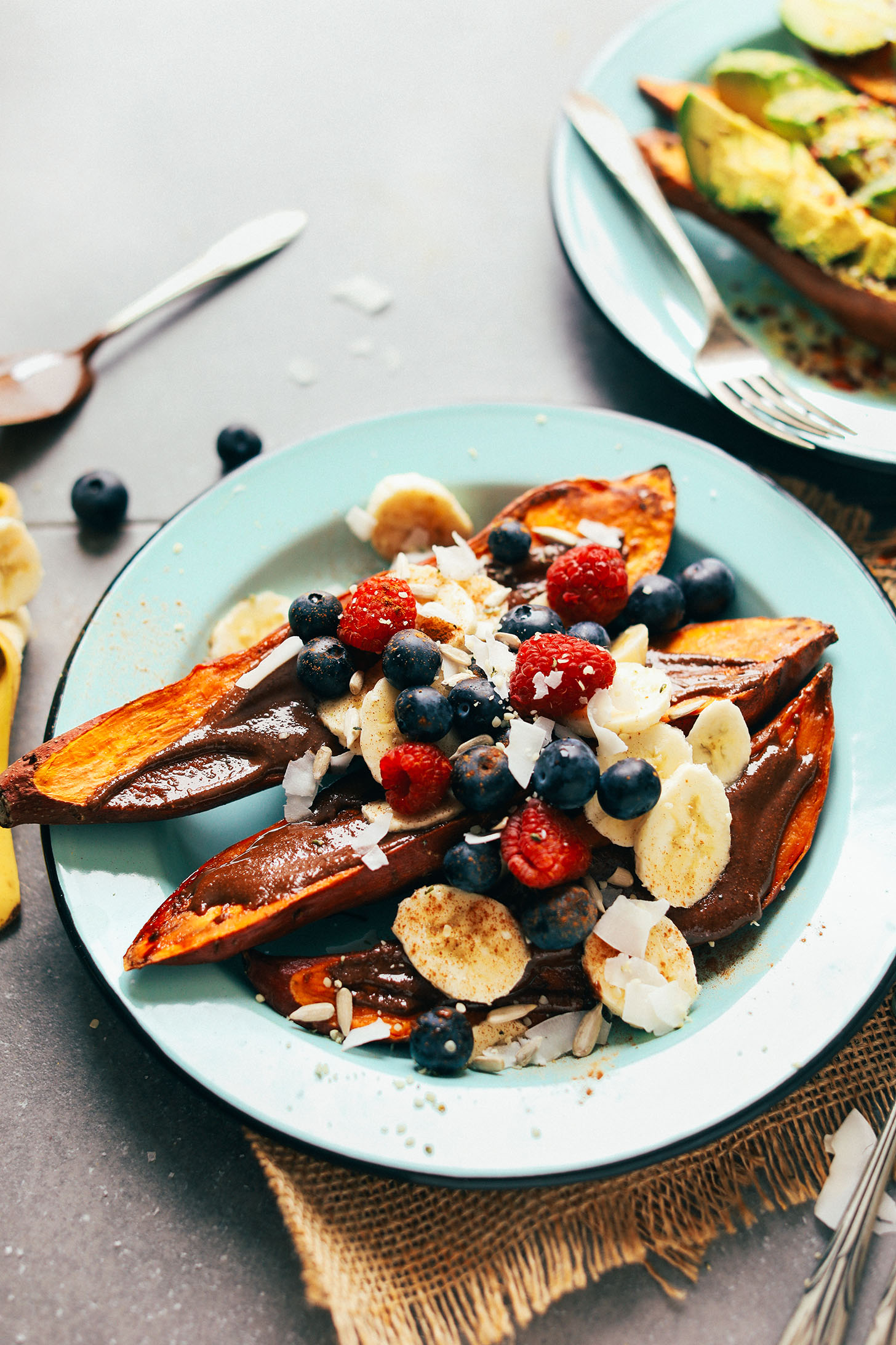 Plate with baked sweet potato topped with vegan melted chocolate, banana, fresh berries, and coconut flakes