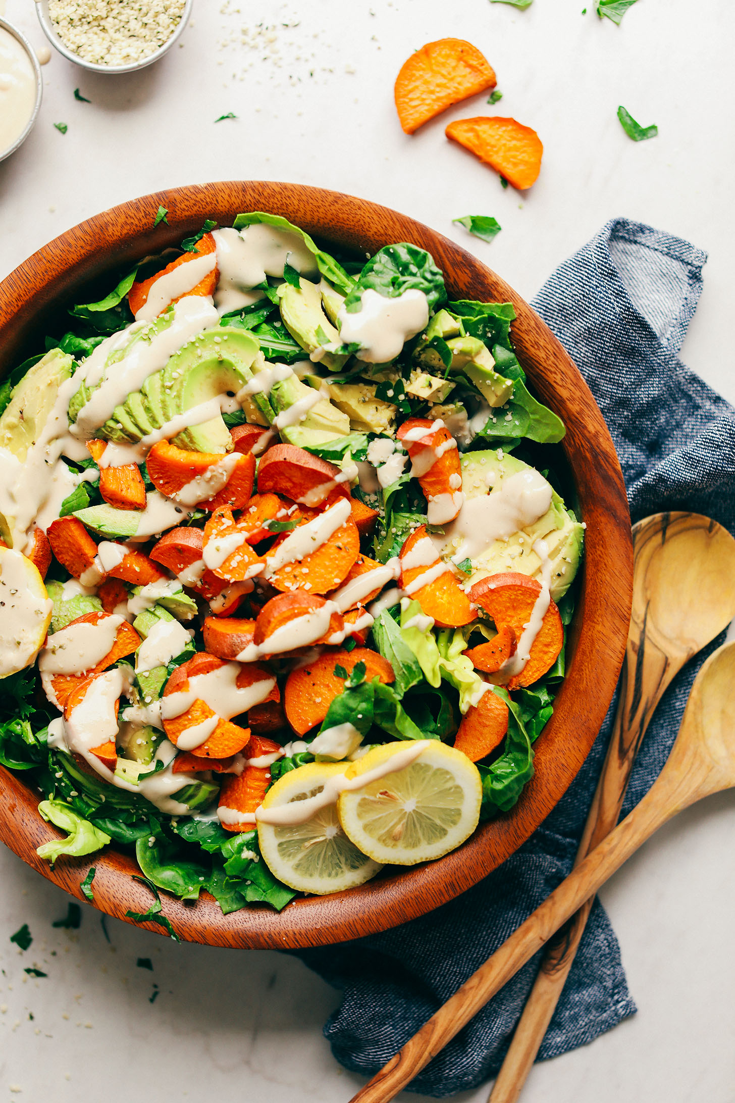 Gluten-free vegan whole meal salad made with greens, avocado, and sweet potato displayed in a wood serving bowl