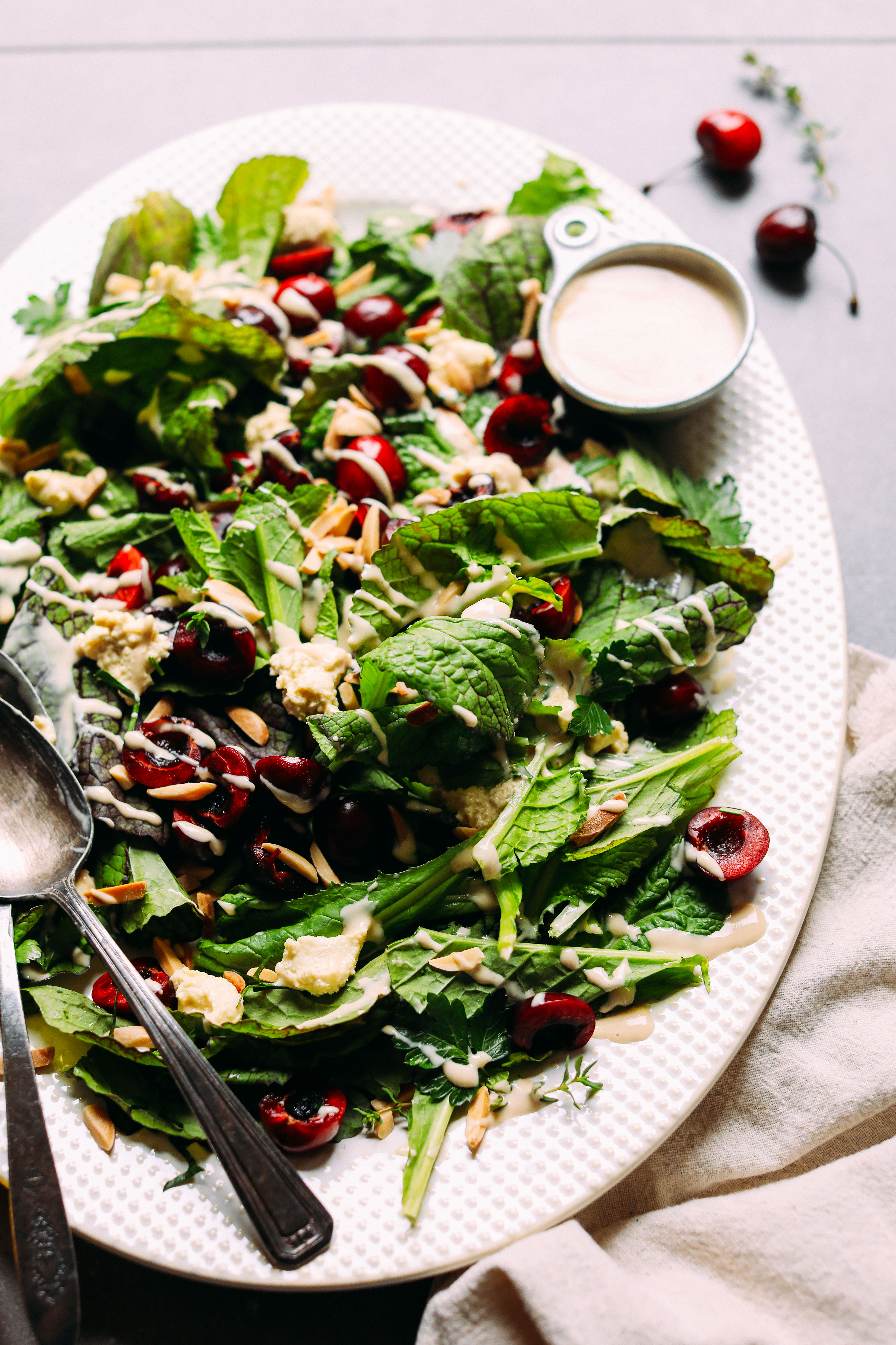 Close up shot highlighting fresh seasonal cherries in our Mustard Green Salad with Cherries, Toasted Almonds, Nut Cheese, and Tahini Dressing